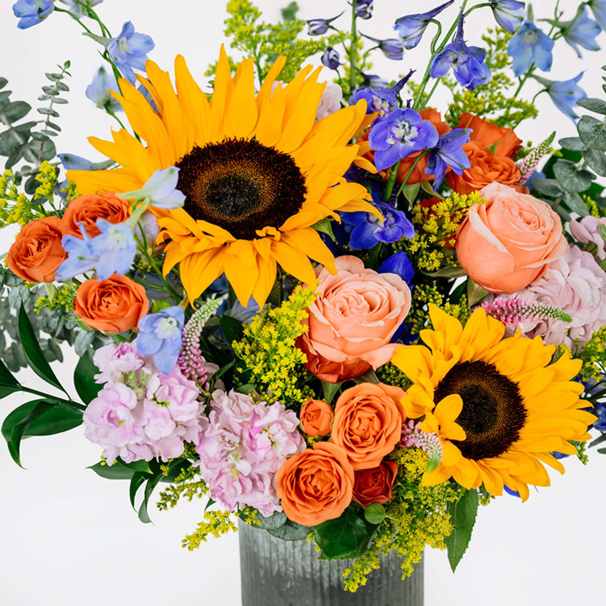 Bouquet with sunflowers, peach roses, and blue flowers in a vase