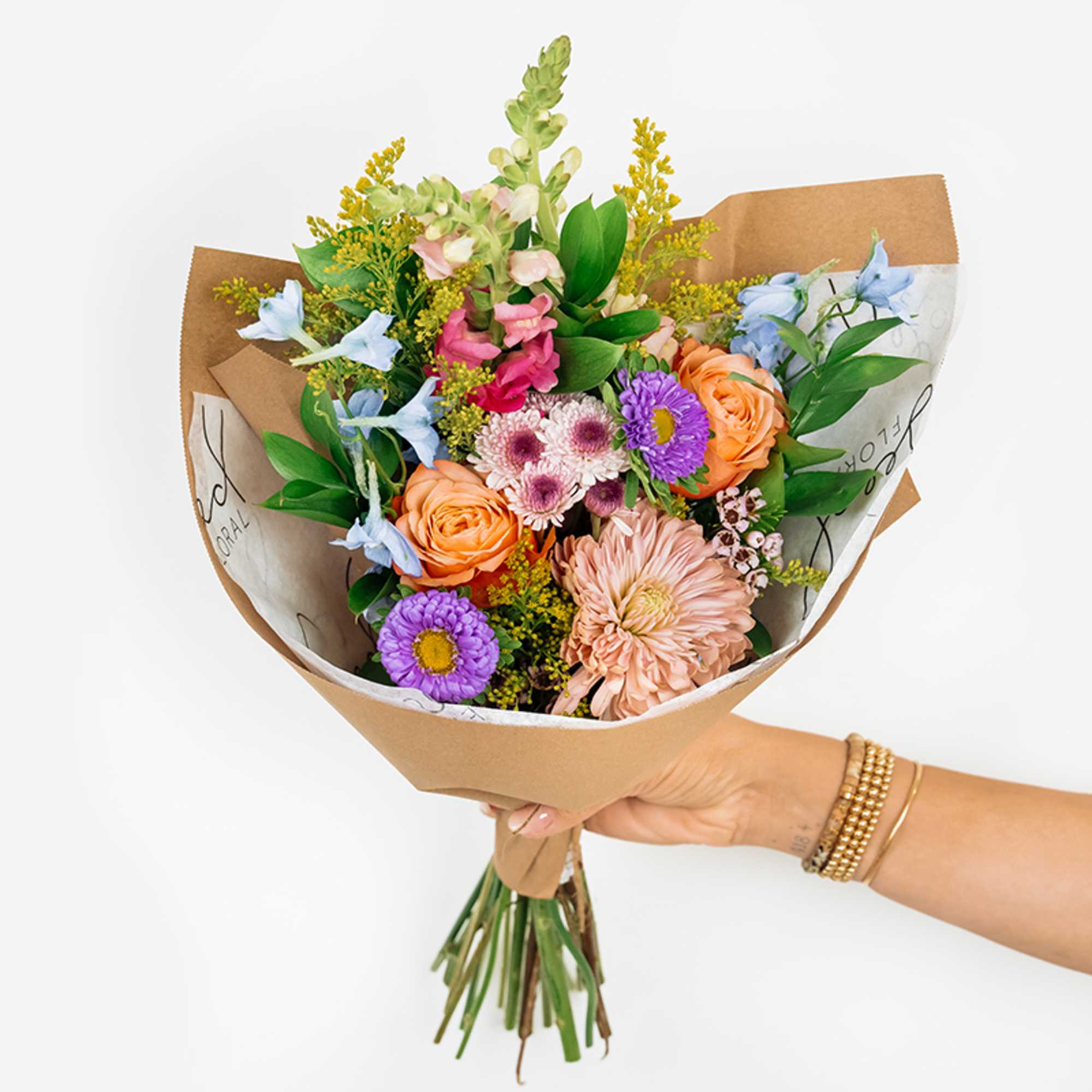 Handheld bouquet of mixed pastel flowers wrapped in brown paper