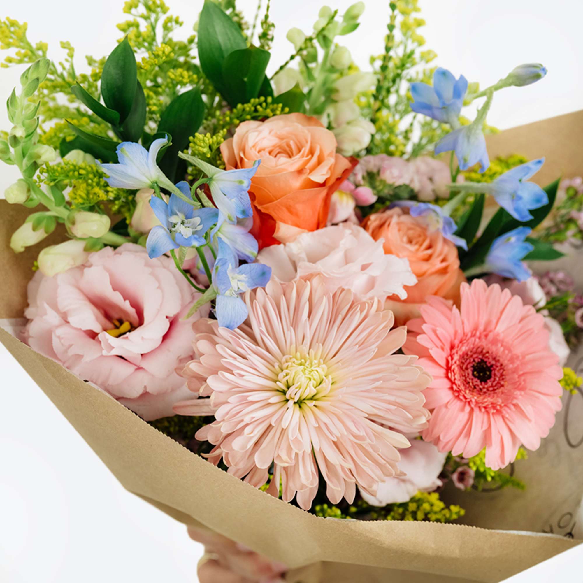 Pastel bouquet with roses, gerbera daisies, and blue flowers in kraft paper