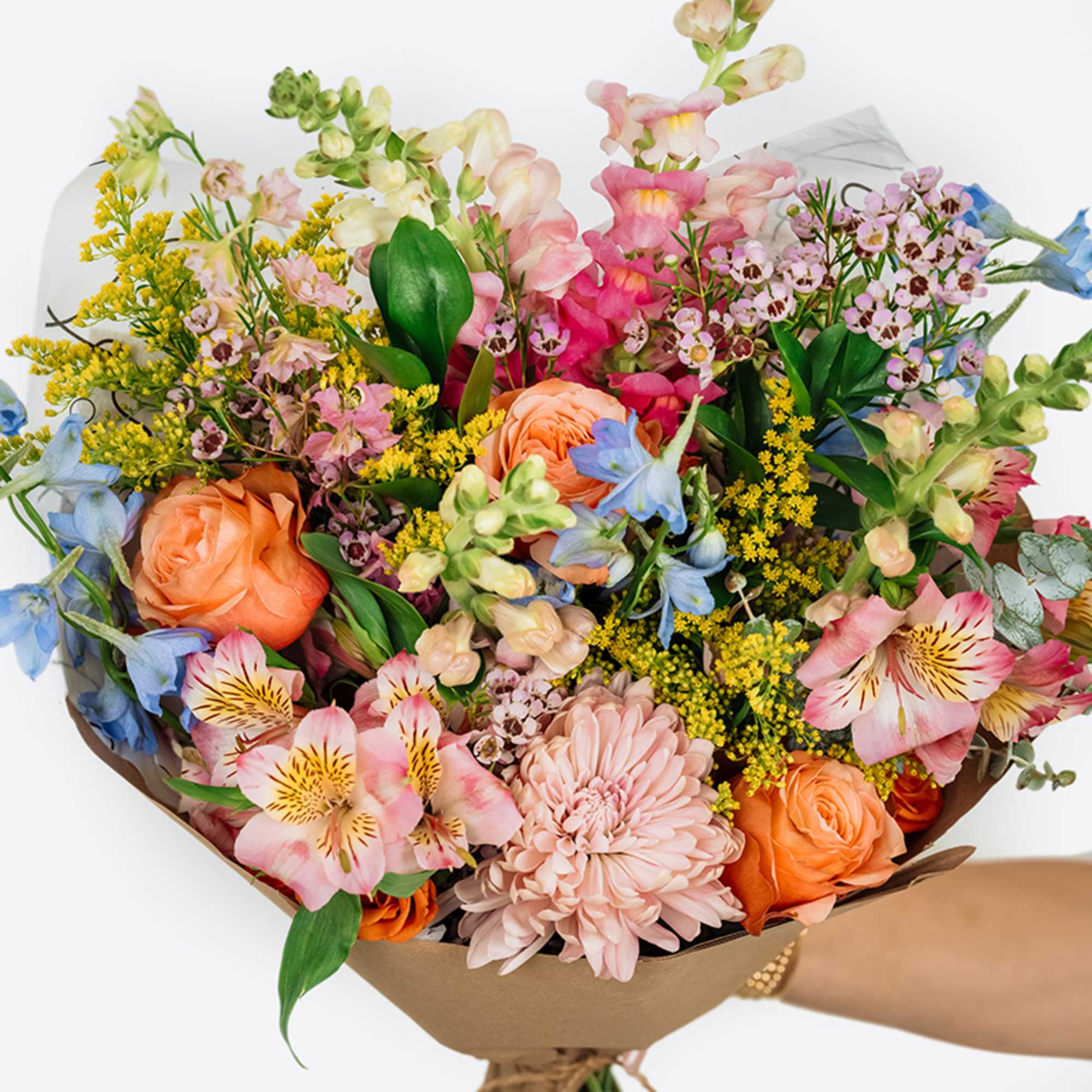Mixed bouquet of peach, pink, blue, and yellow flowers wrapped in brown paper