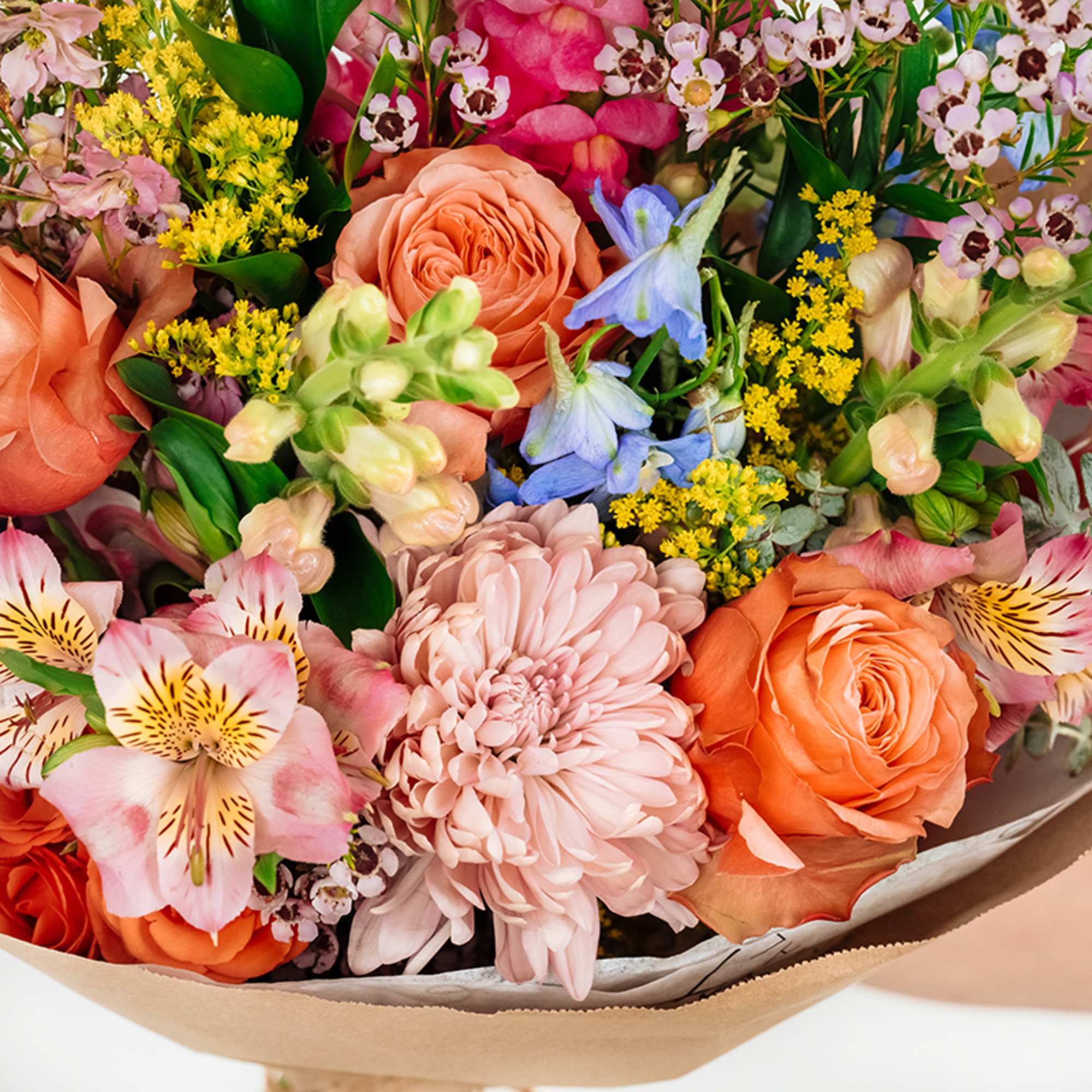 Mixed bouquet of orange roses, pink blooms, and pastel flowers wrapped in paper
