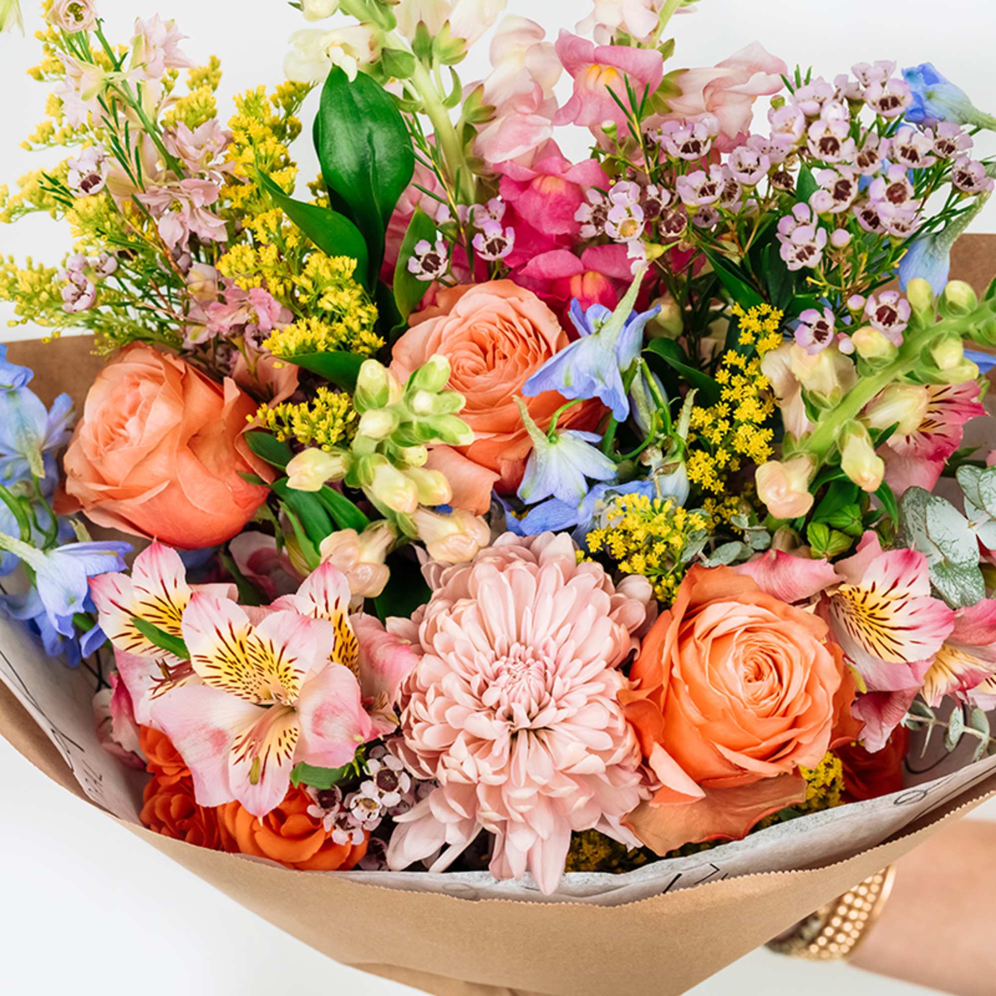 Mixed bouquet of peach, pink, and blue flowers wrapped in brown paper