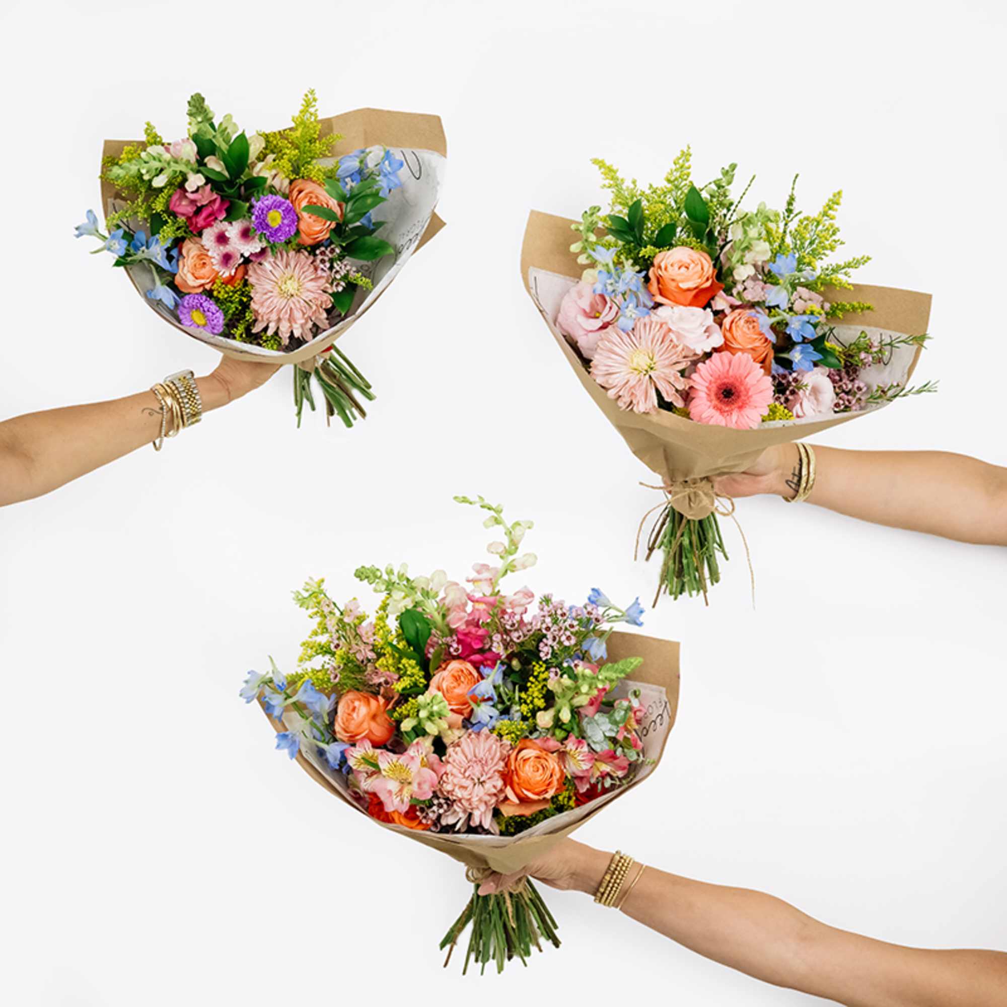 Three hand-held mixed flower bouquets wrapped in kraft paper