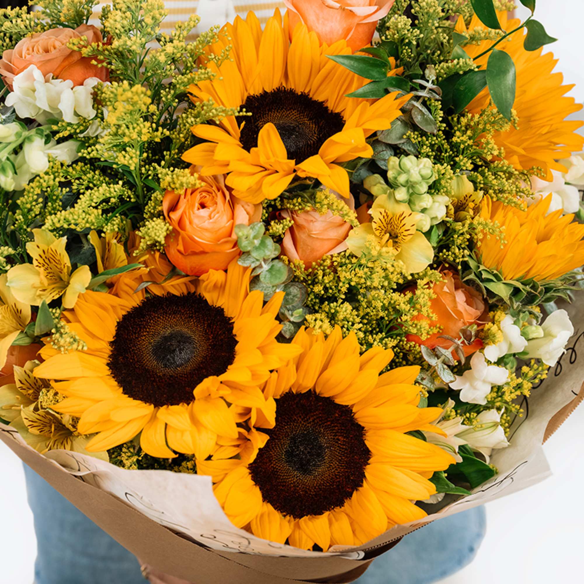 Bouquet of sunflowers, peach roses, and white blooms wrapped in paper