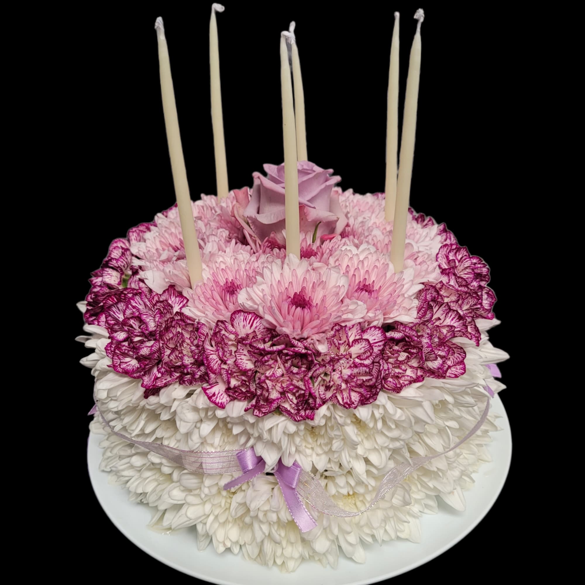 Round floral cake with pink and white flowers and tall candles