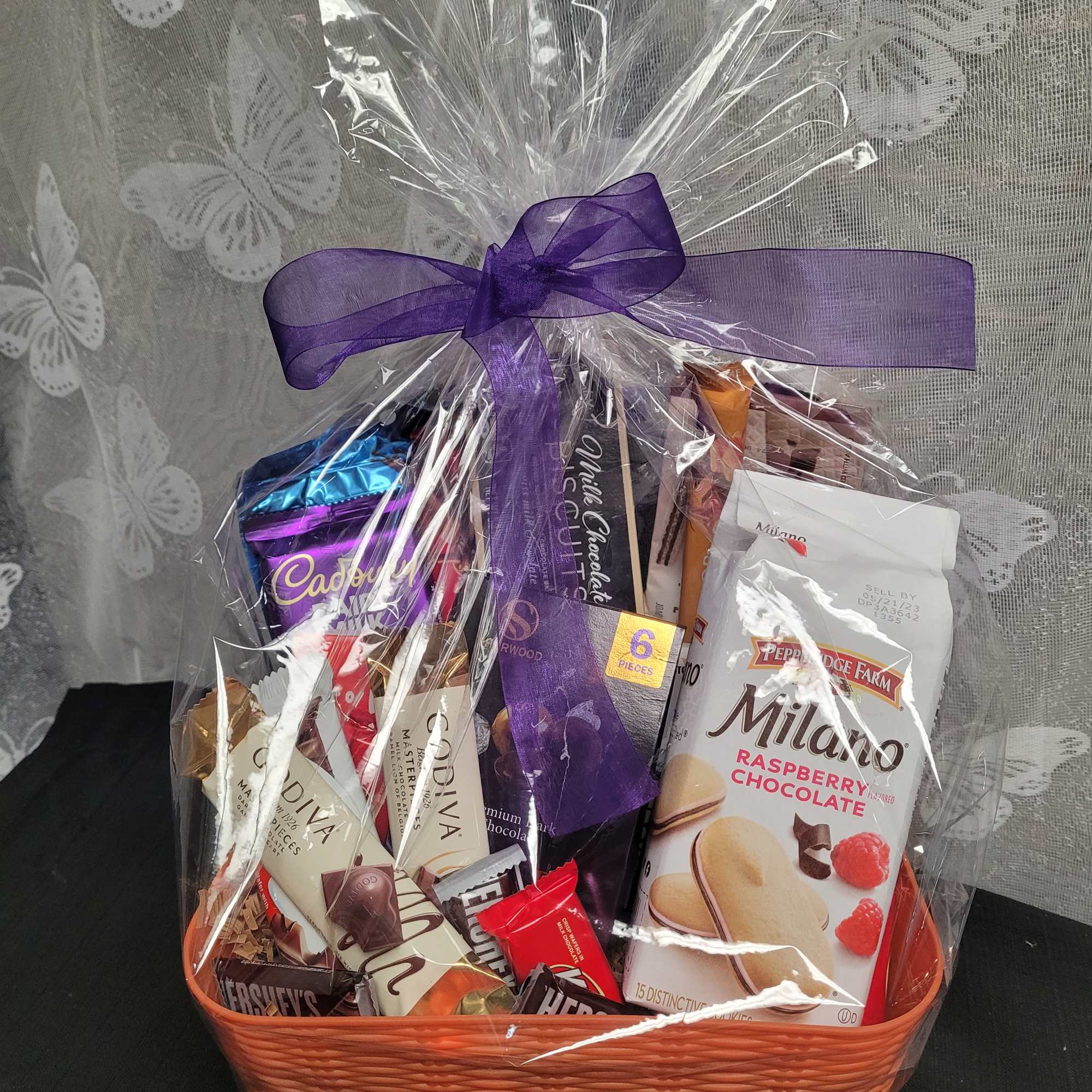 Basket of assorted chocolates wrapped in clear cellophane with a purple bow