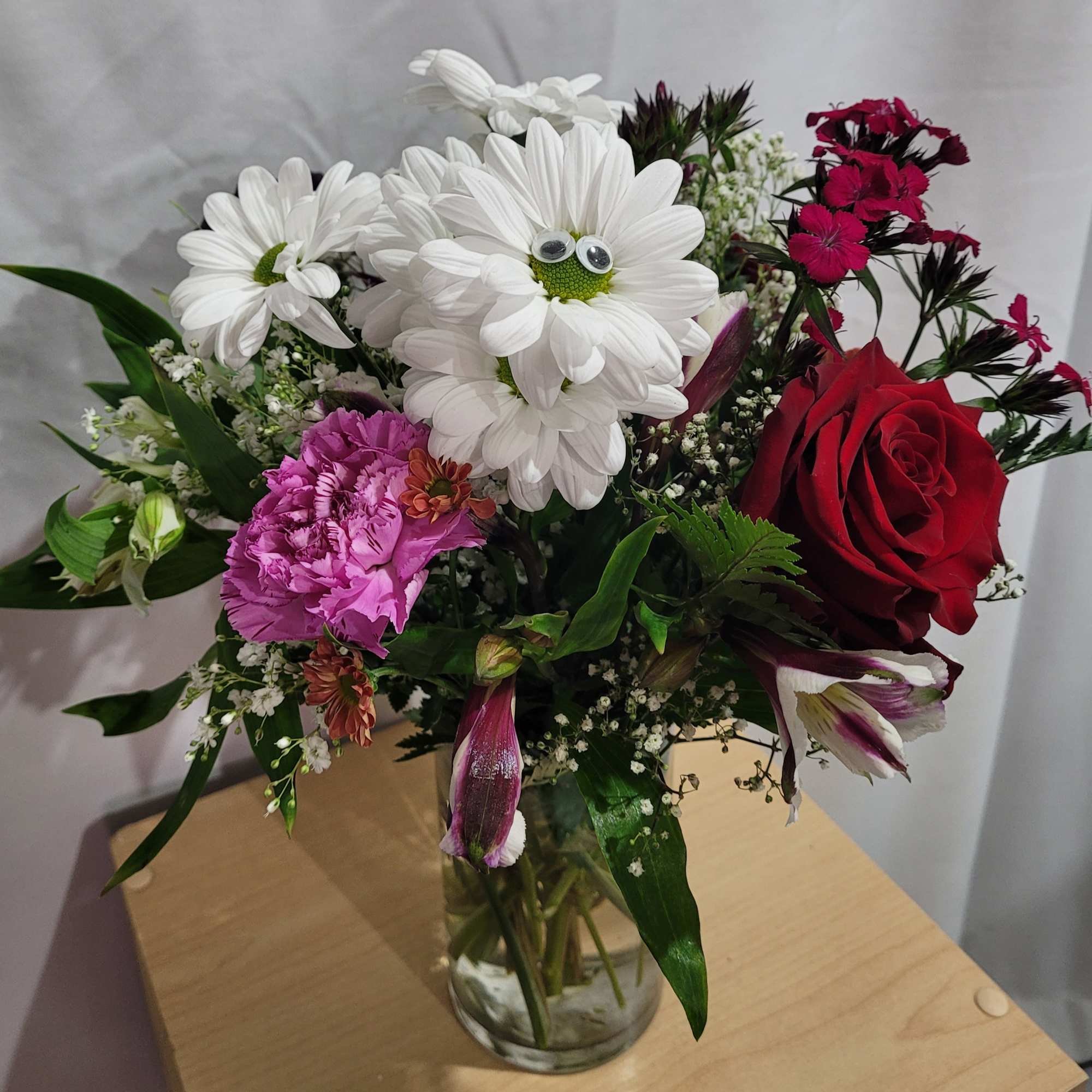 Bouquet of mixed flowers in a glass vase with a red rose and white daisies