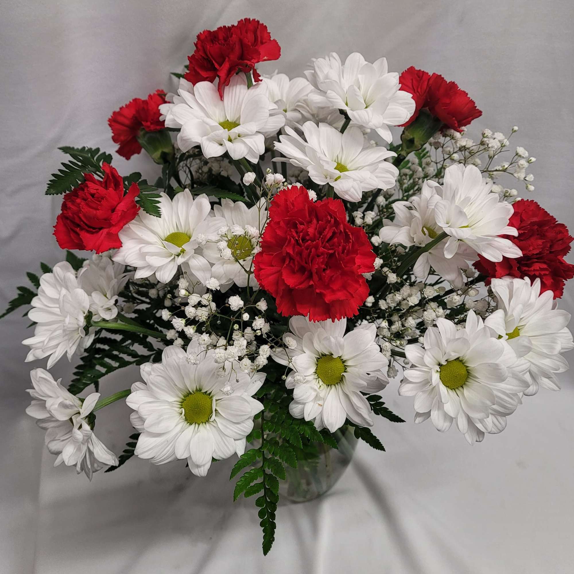Bouquet of red carnations and white daisies in a clear glass vase
