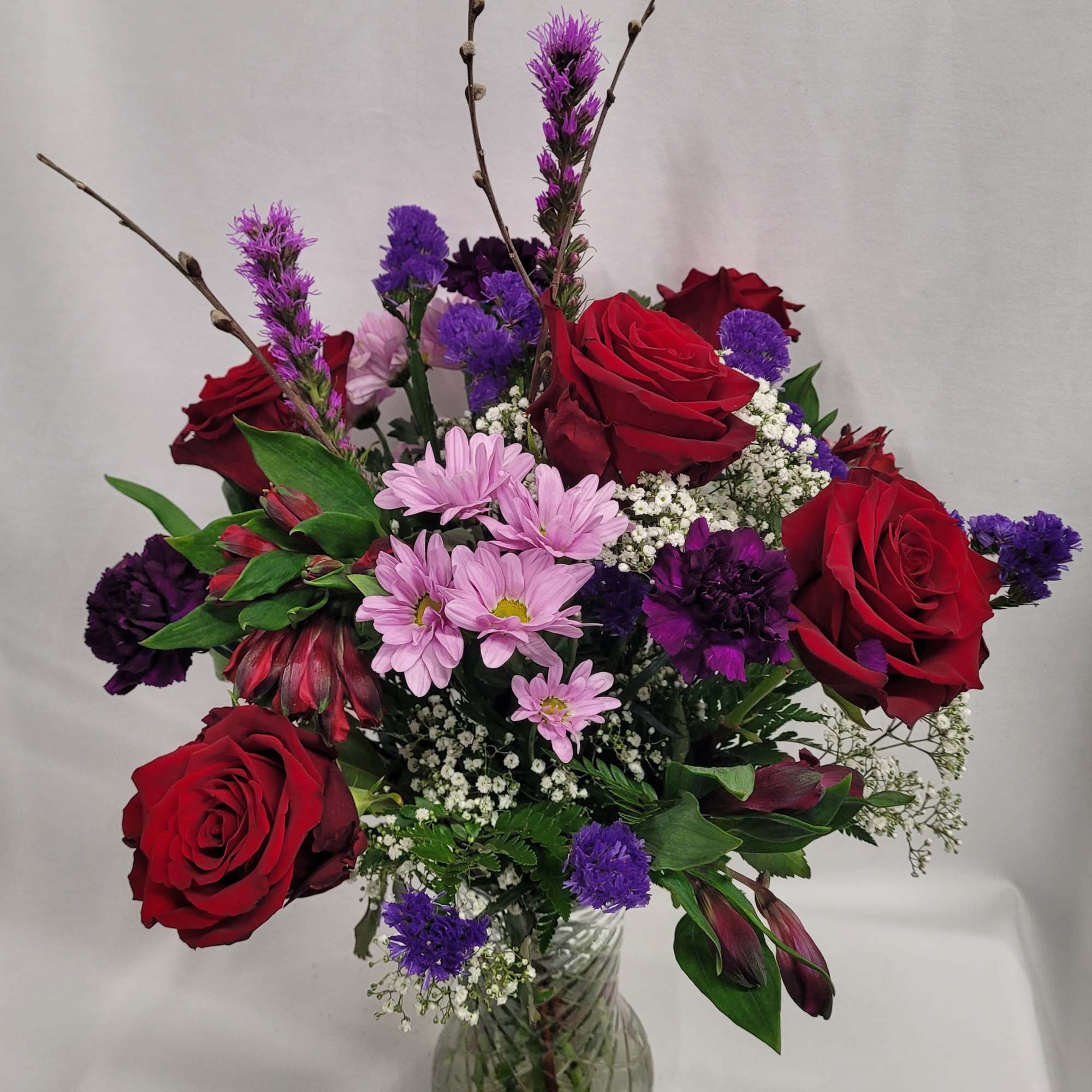 Bouquet of red roses, pink daisies, and purple flowers in a glass vase