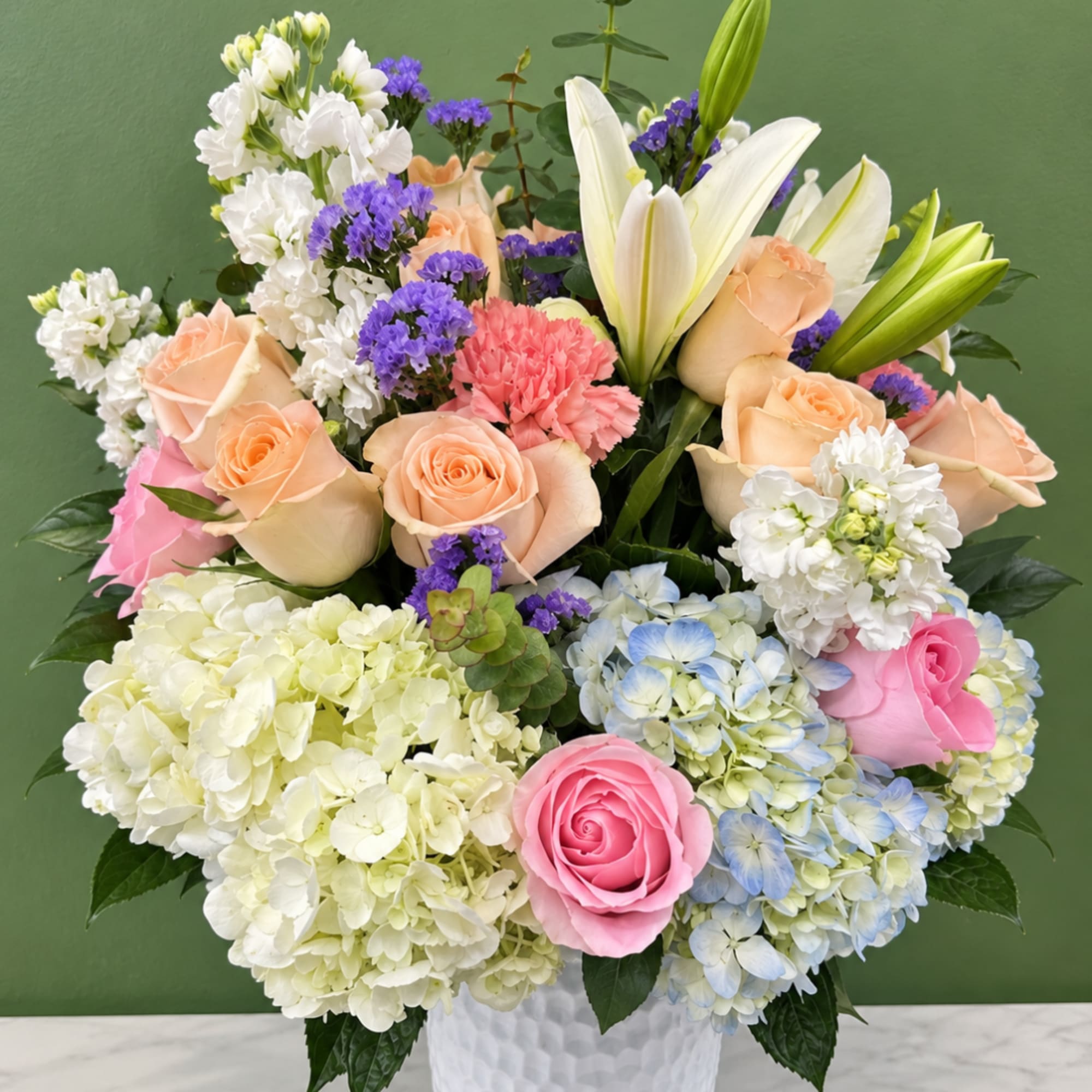 Mixed bouquet of roses, lilies, hydrangeas, and carnations in a white vase