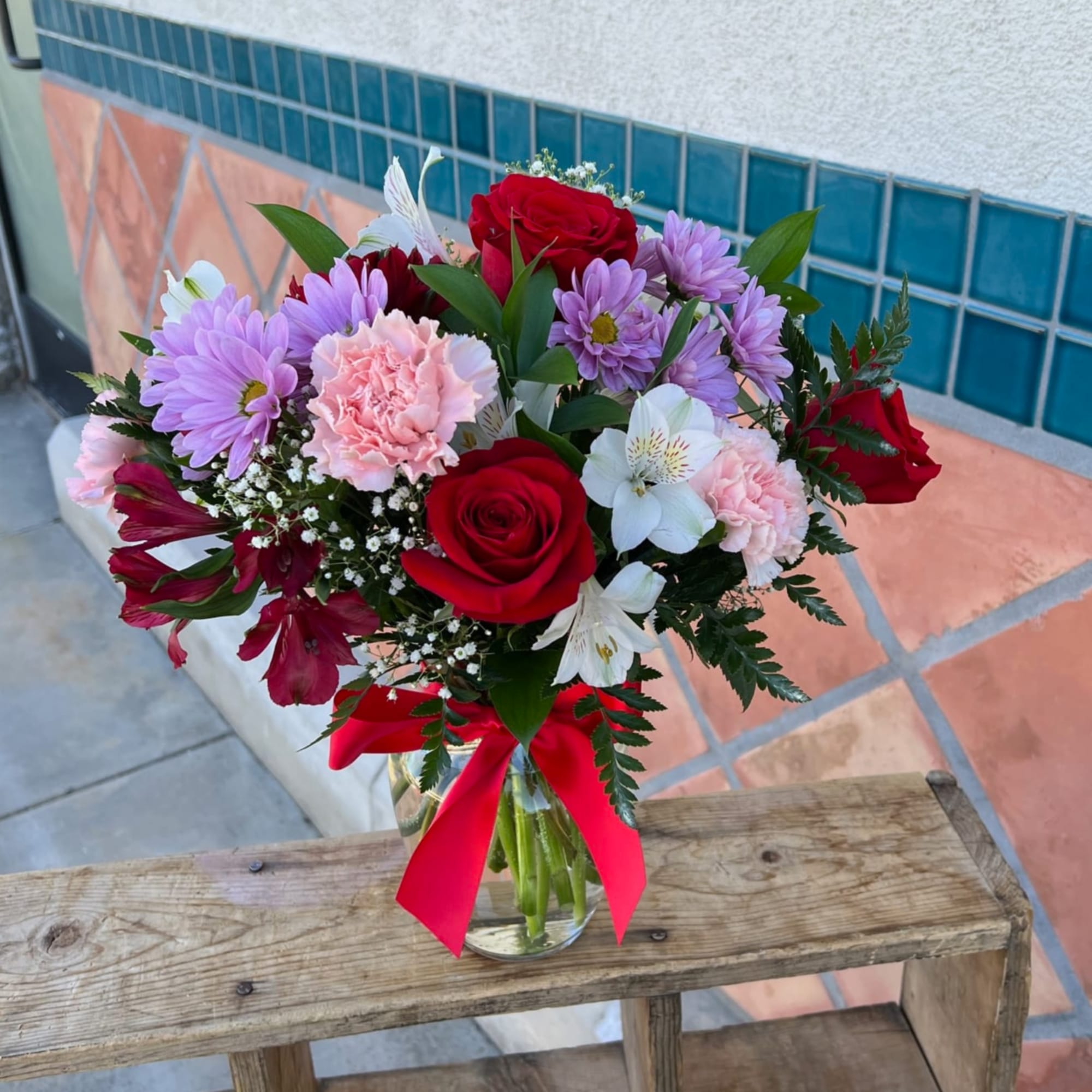 Bouquet of red roses, purple daisies, and pink carnations in a glass vase