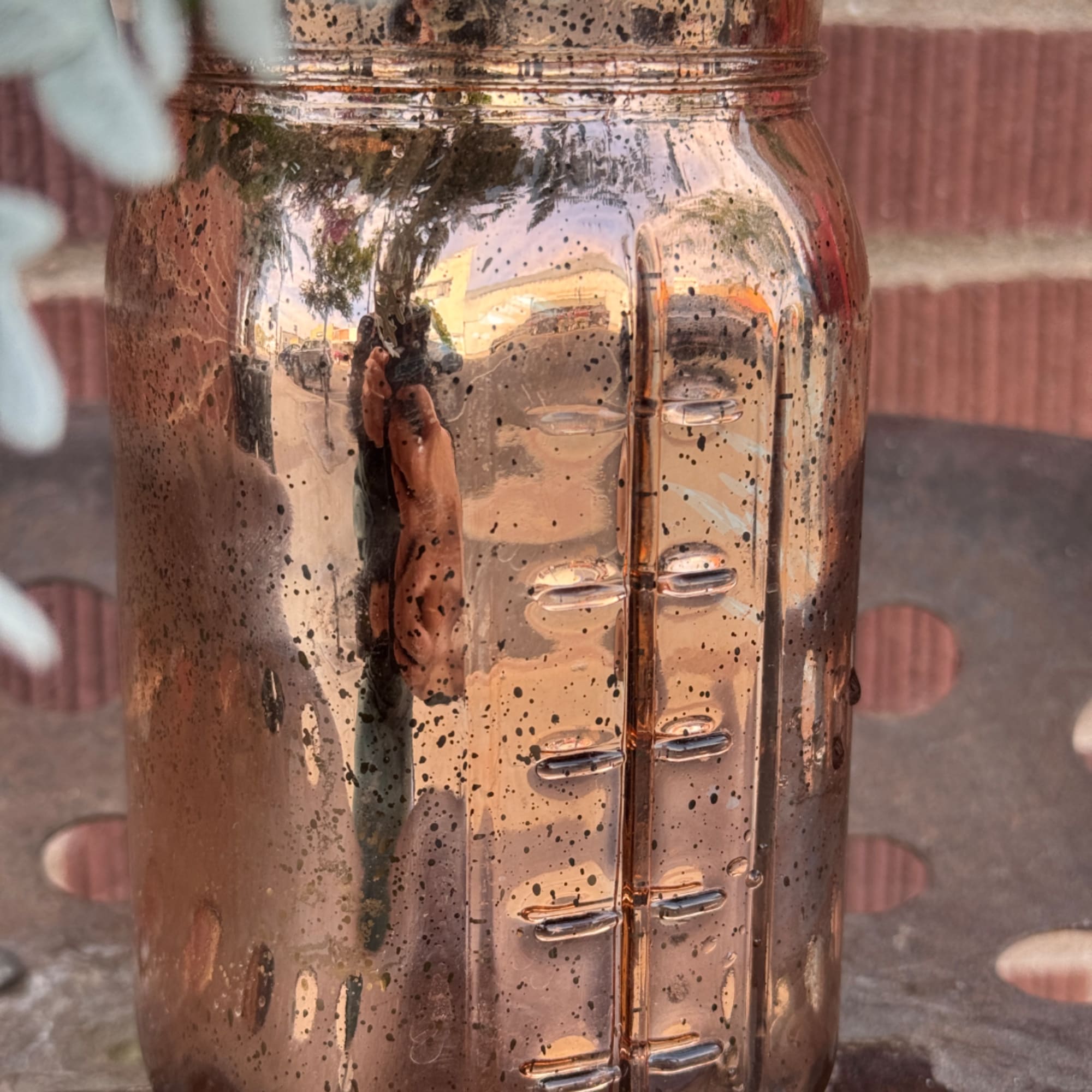 Copper-toned reflective vase with a face design and blurred flowers at the edge