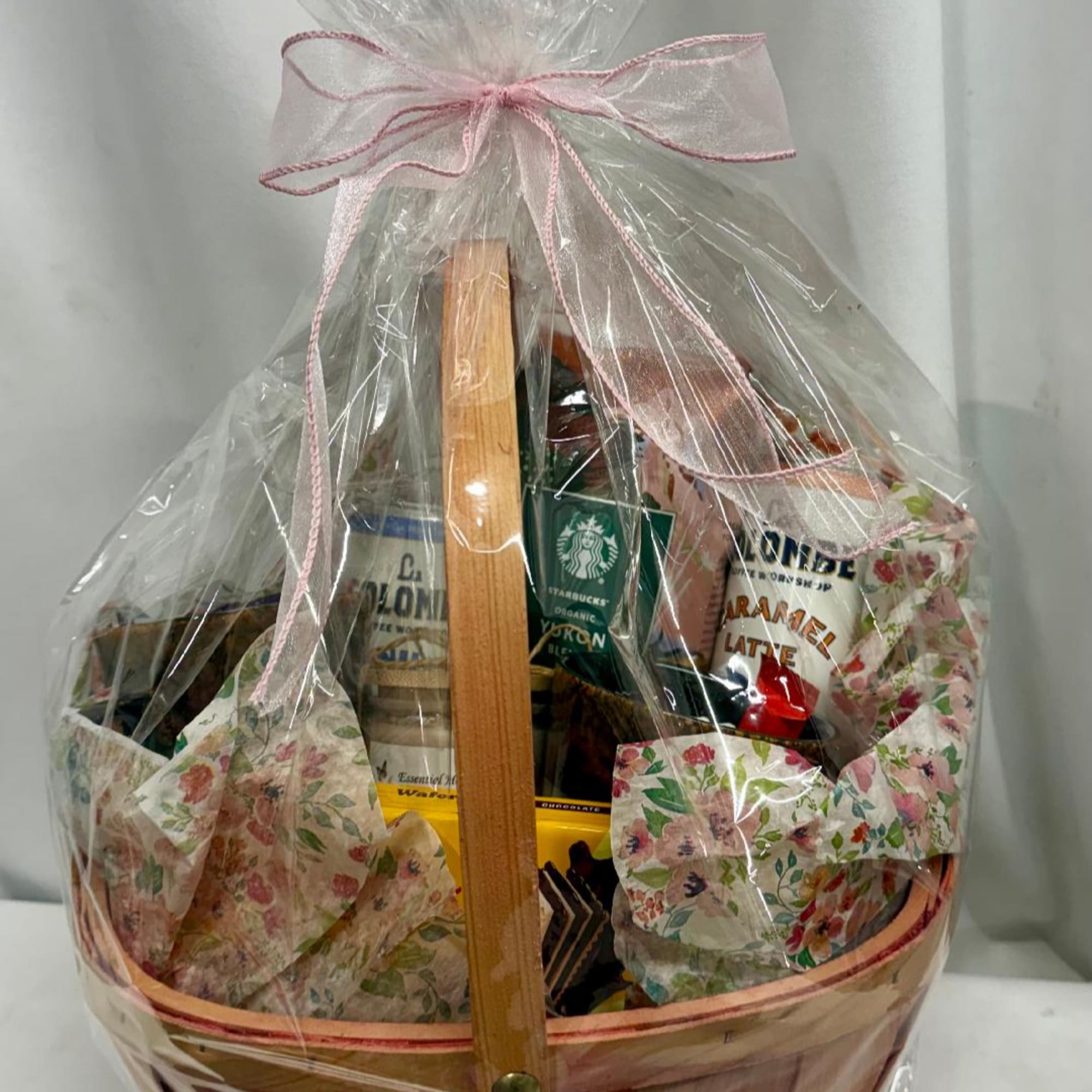Gift basket wrapped in clear plastic with a pink ribbon