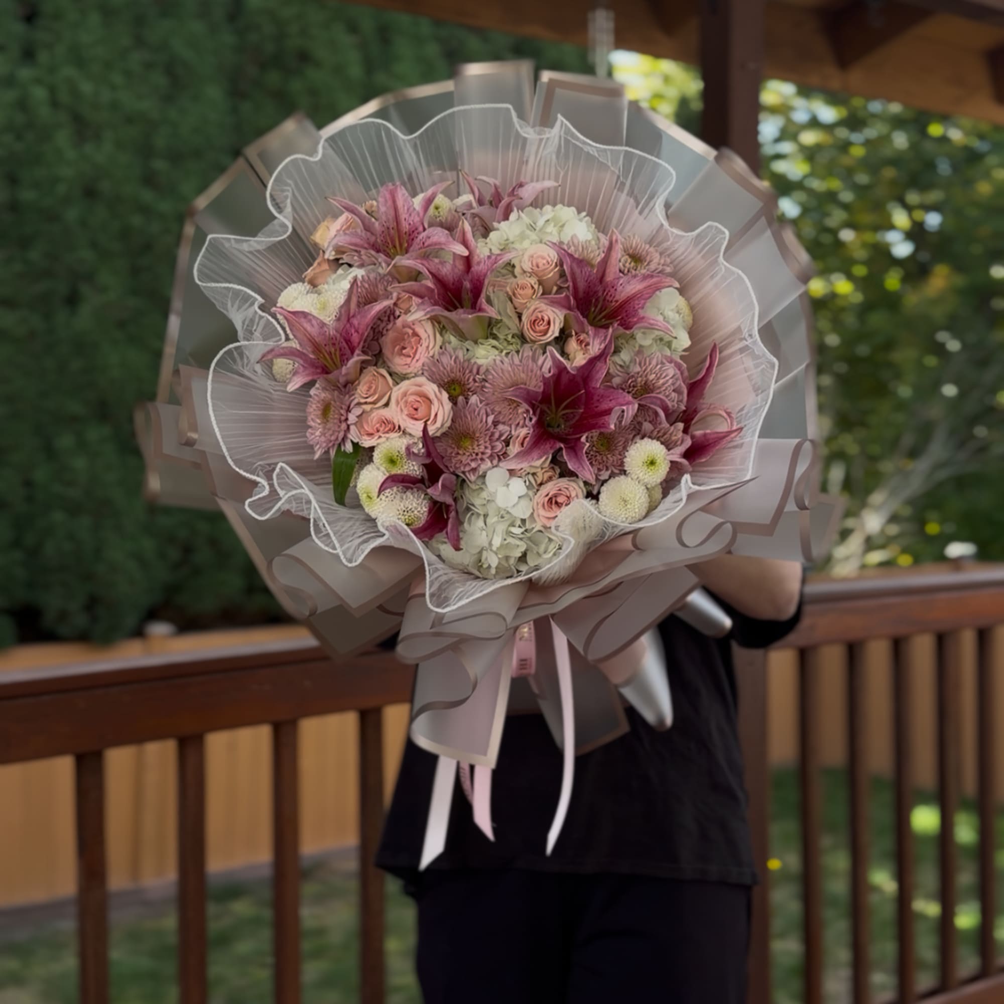 Handheld bouquet of pink lilies, roses, and chrysanthemums wrapped in sheer paper