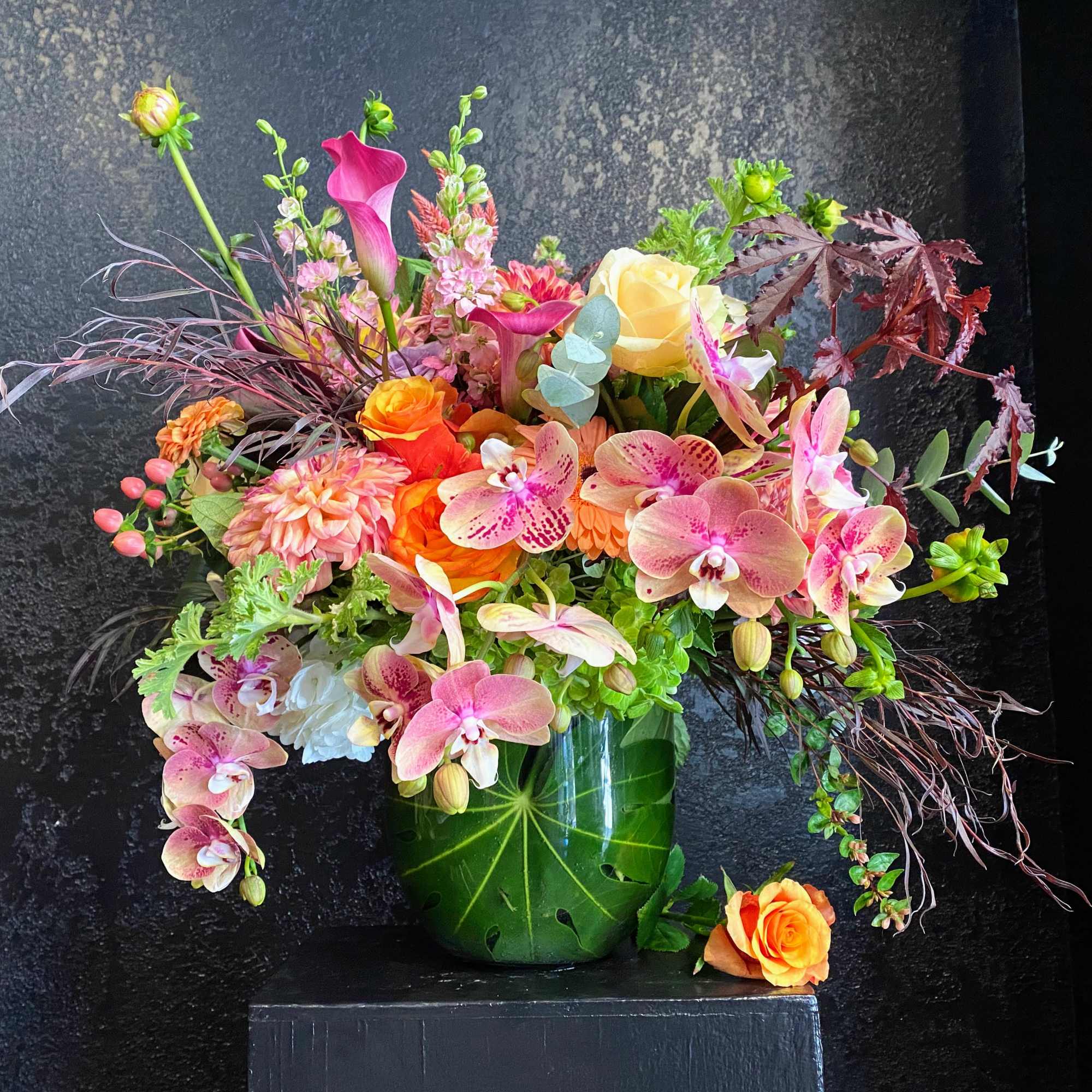 Mixed bouquet of pink orchids, roses, and calla lilies in a green vase