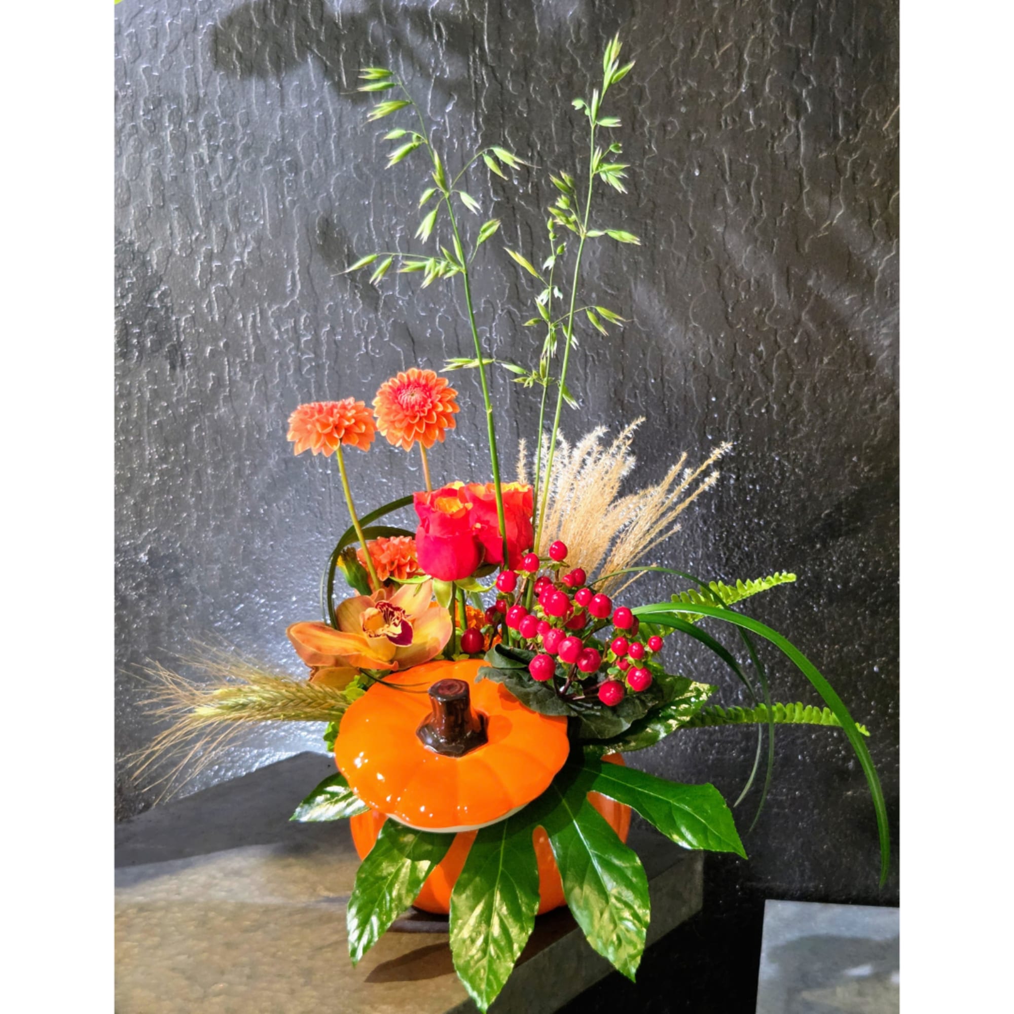 Orange floral arrangement in a pumpkin-shaped container with tall stems