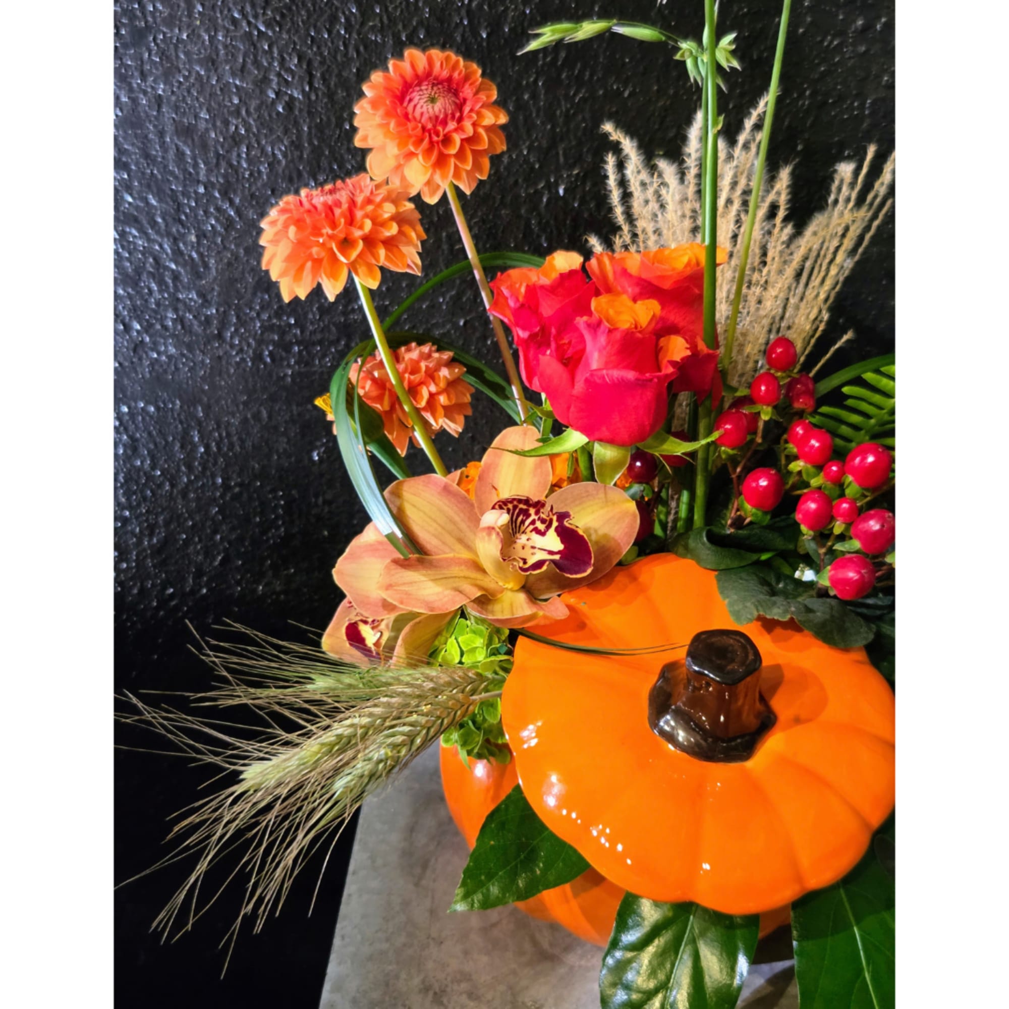 Orange floral arrangement in a pumpkin container with roses and orchids