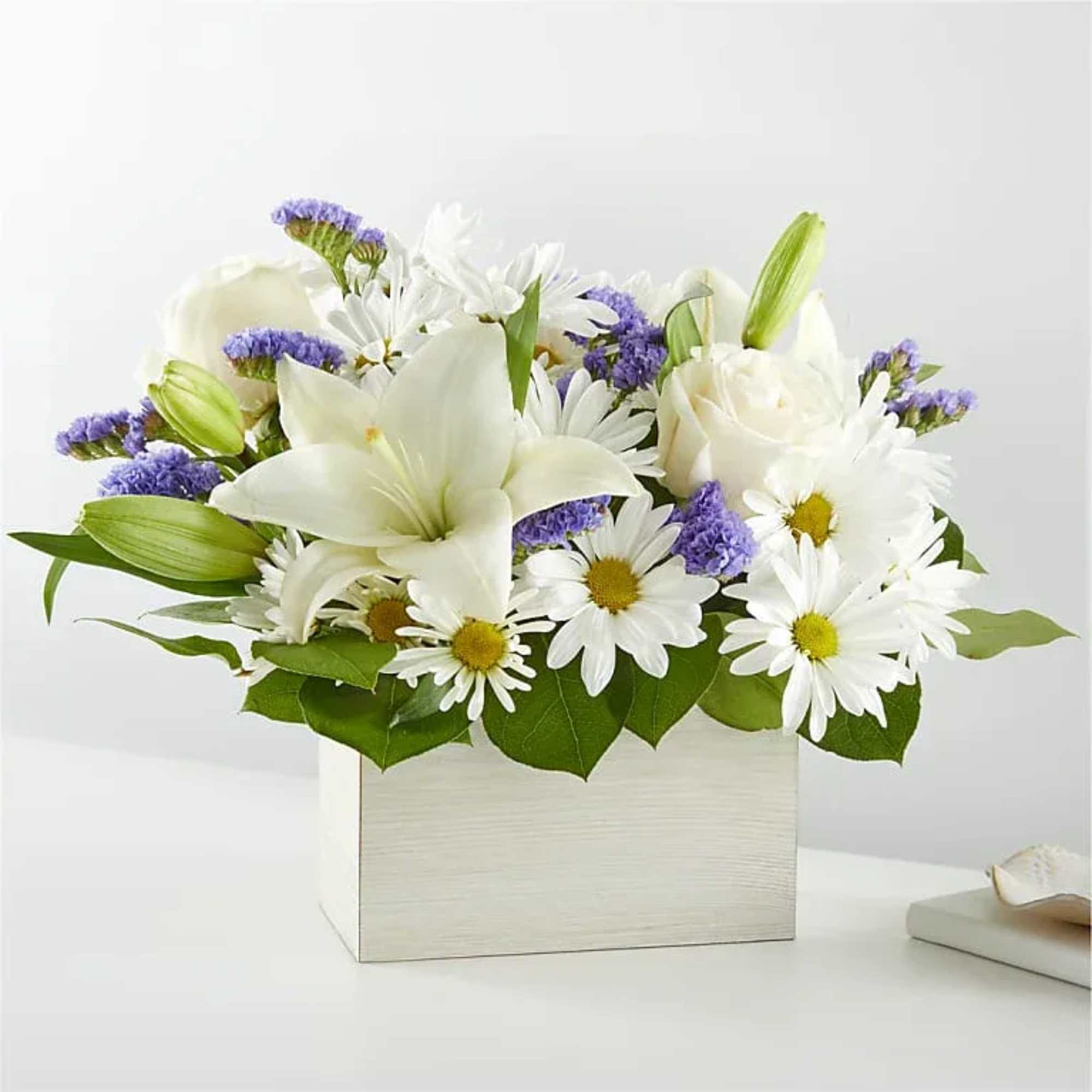White lilies and daisies arranged in a square white box with purple accents
