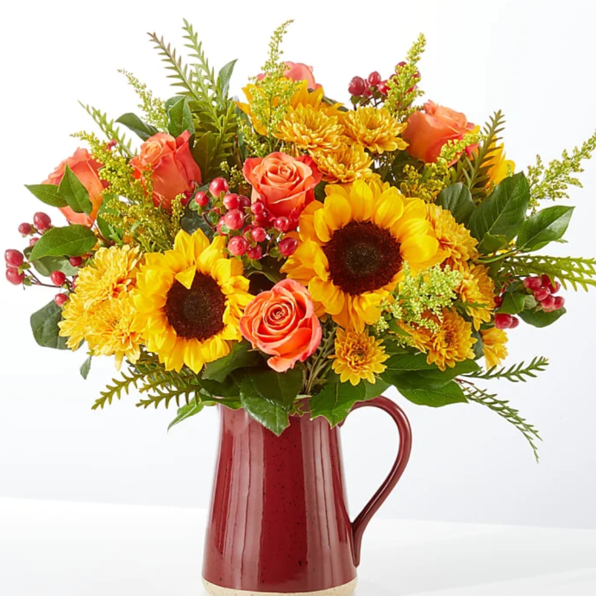 Bouquet of sunflowers, orange roses, and yellow mums in a red pitcher vase