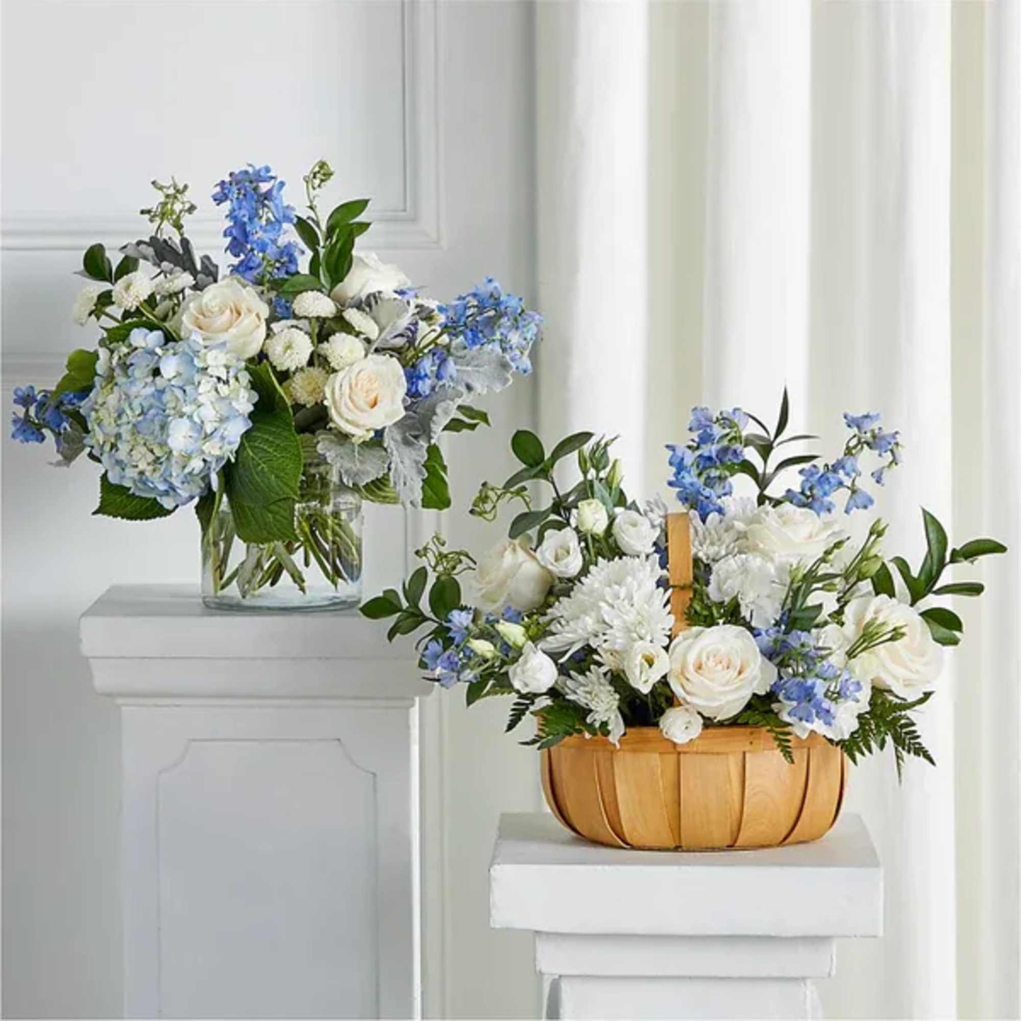 Two white and blue flower arrangements, one in a glass vase and one in a wooden basket.