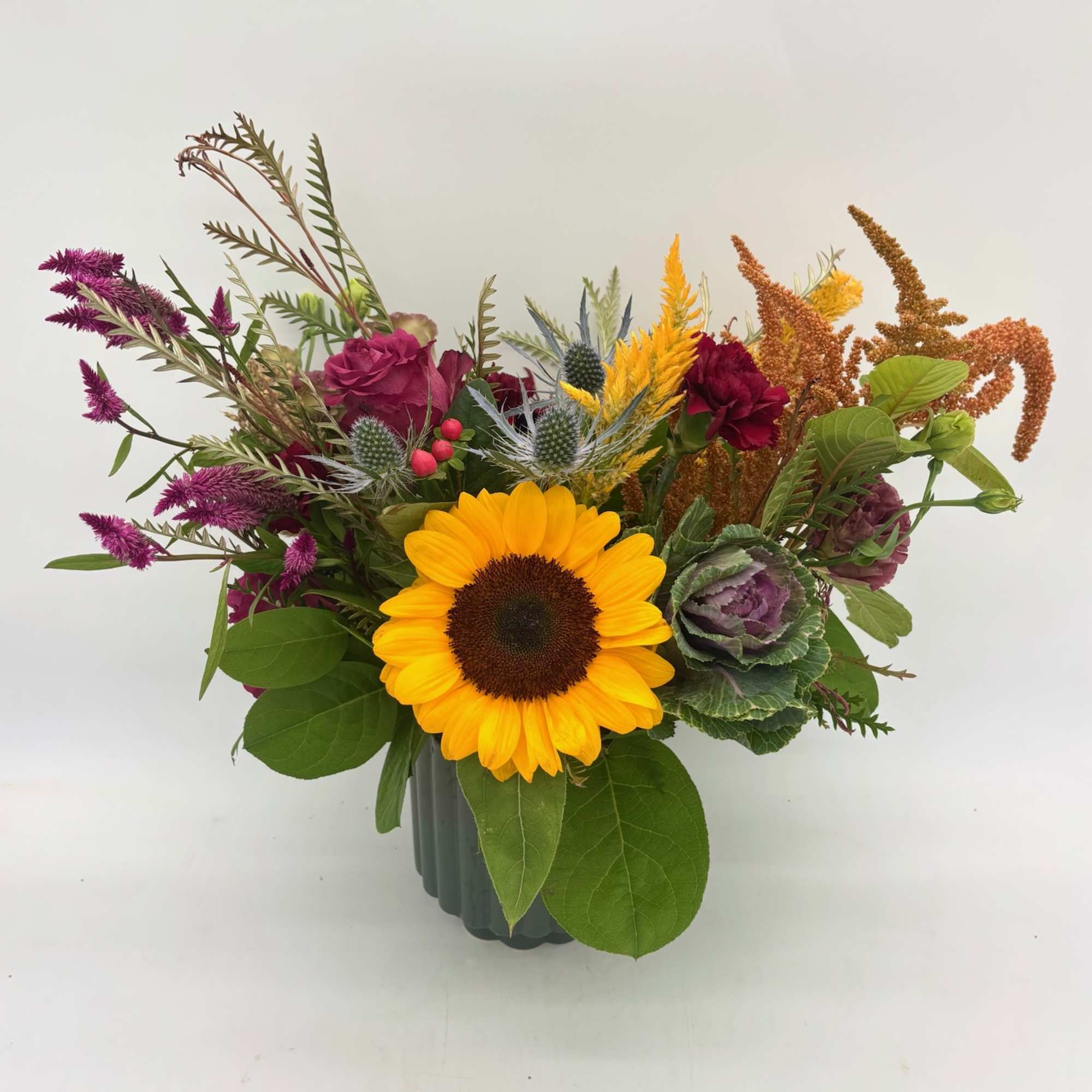 Mixed bouquet with a sunflower, purple blooms, and a dark vase