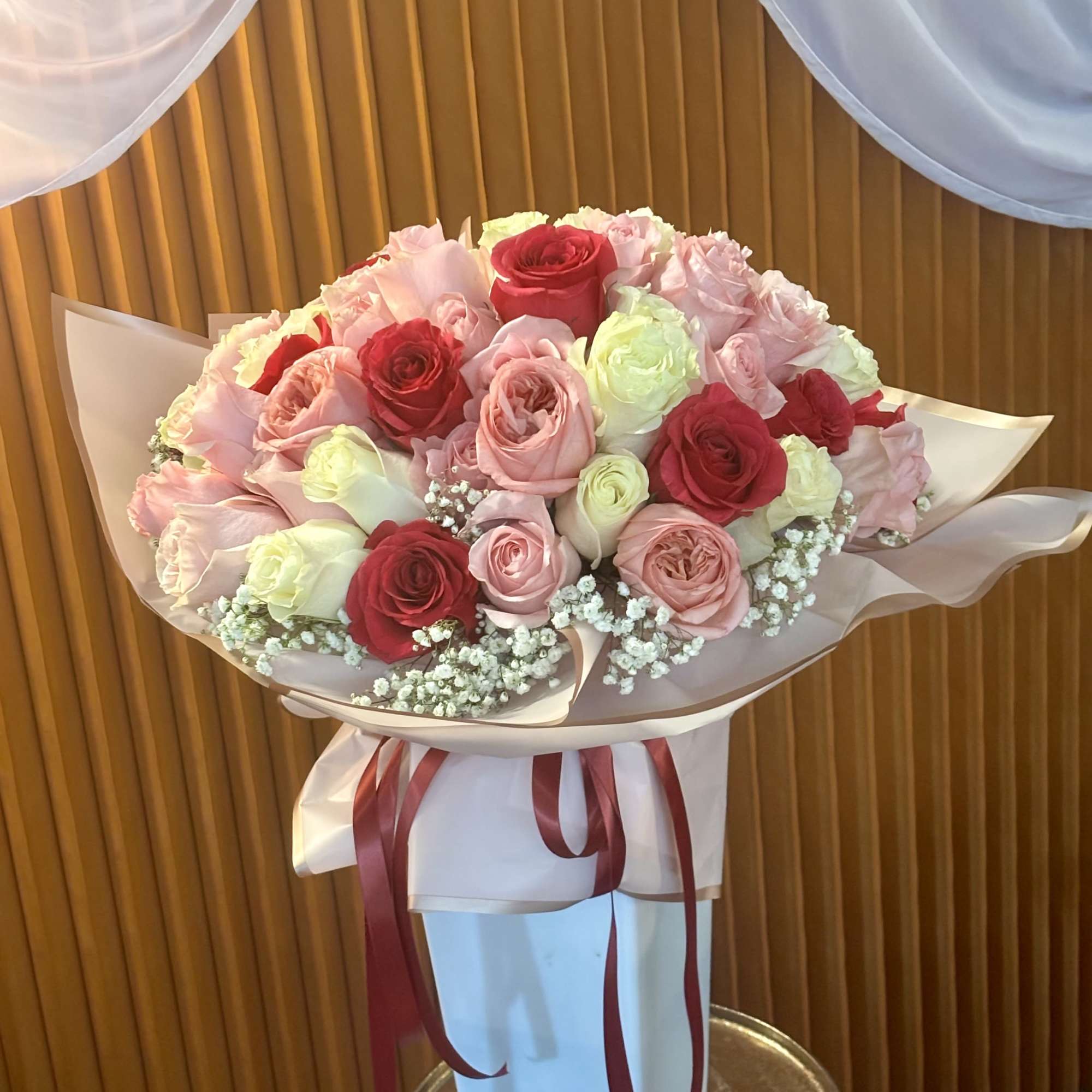 Bouquet of pink, red, and white roses wrapped in paper with ribbon