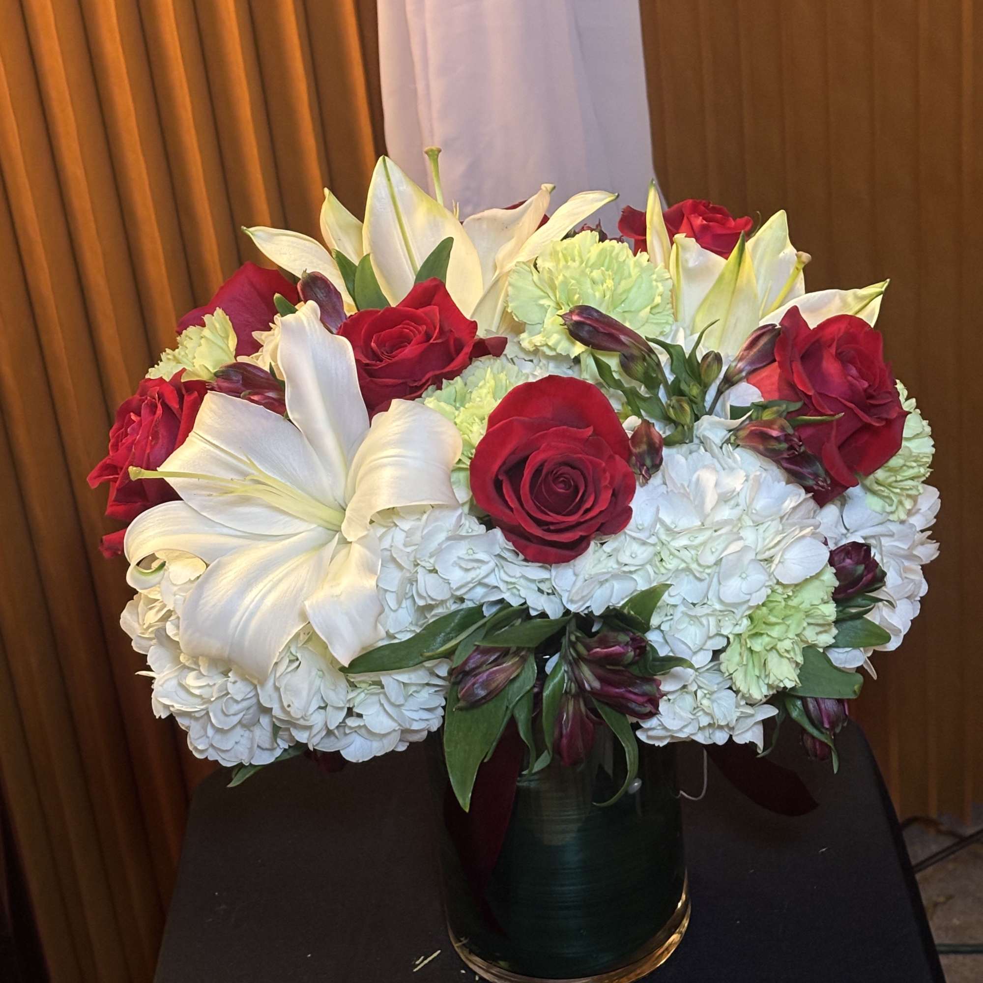 Bouquet of red roses, white lilies, and pale hydrangeas in a glass vase