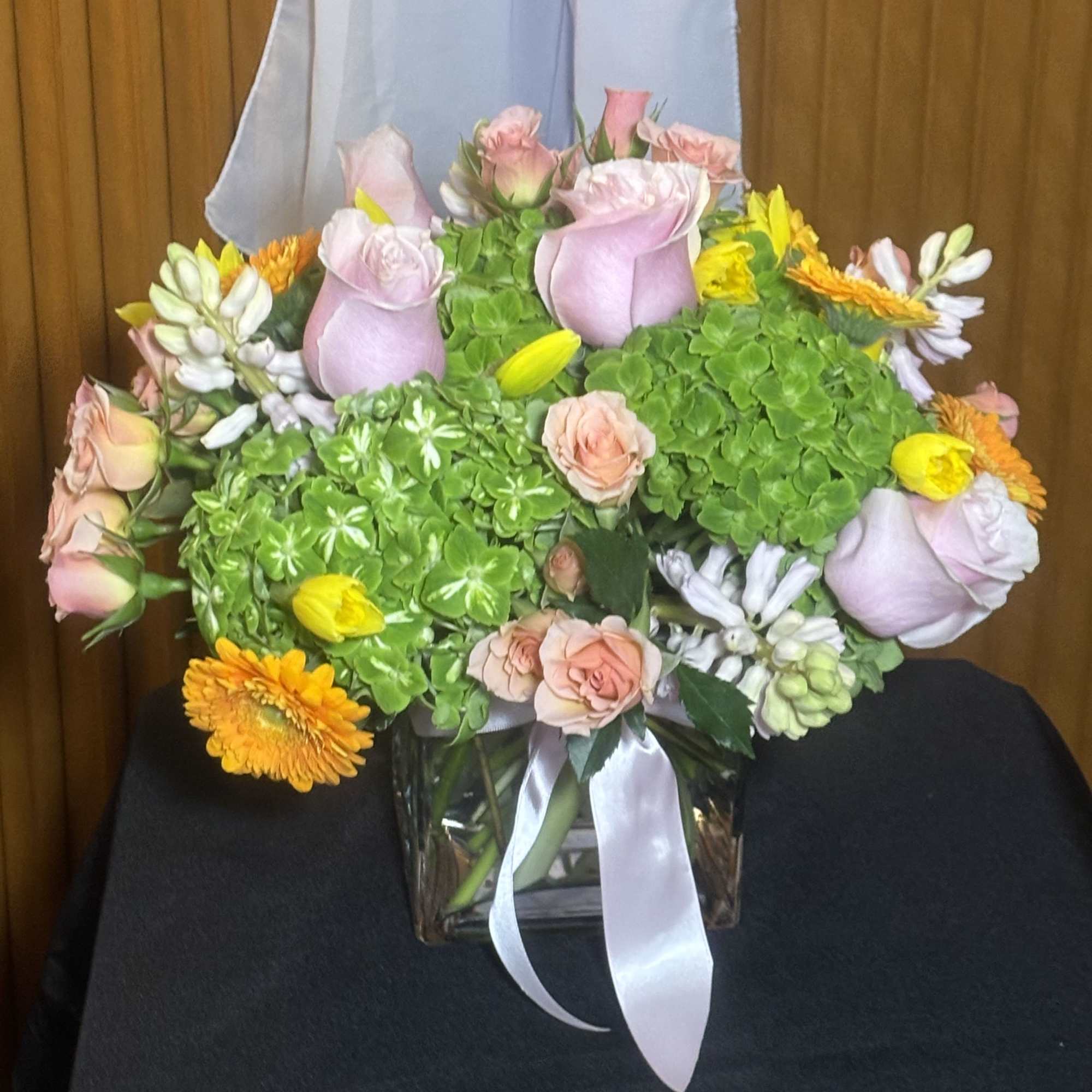 Pink roses and yellow-orange flowers in a glass vase with a white ribbon