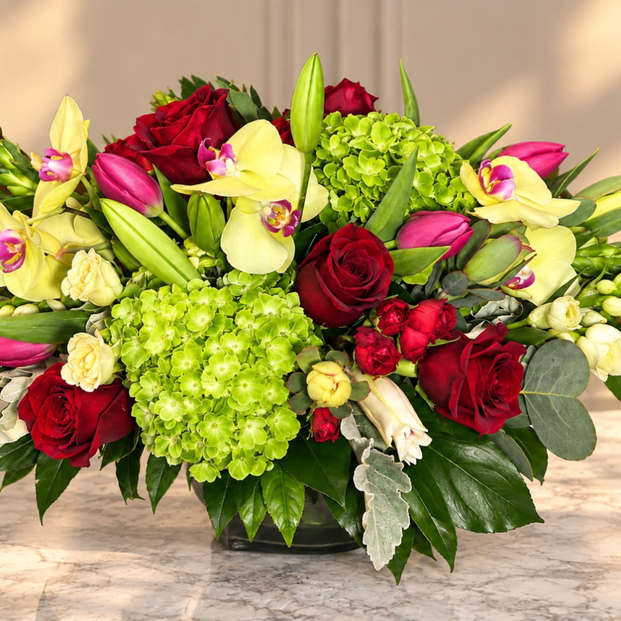 Bouquet of red roses, yellow orchids, and green hydrangeas in a low vase