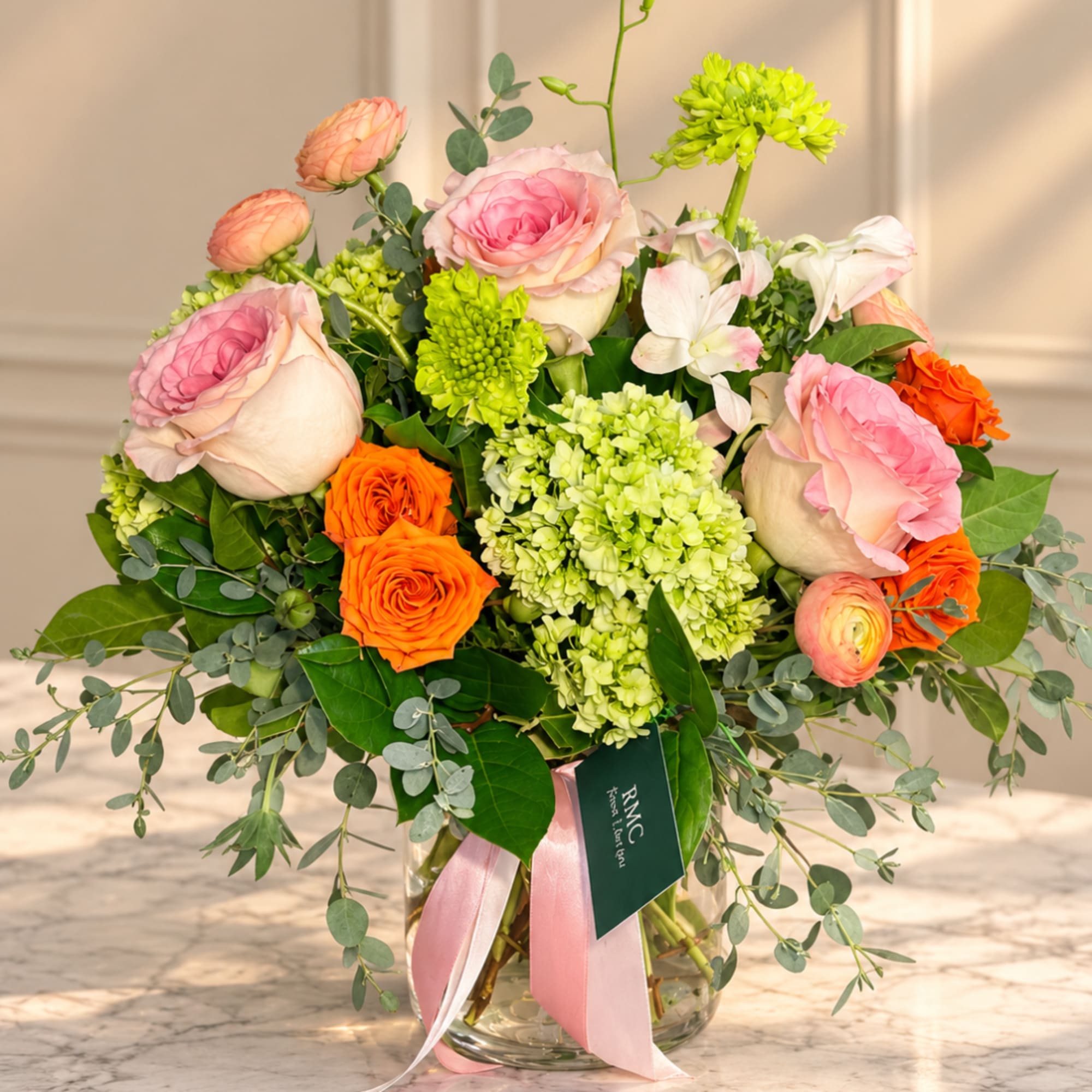 Pink and orange roses with green blooms in a glass vase
