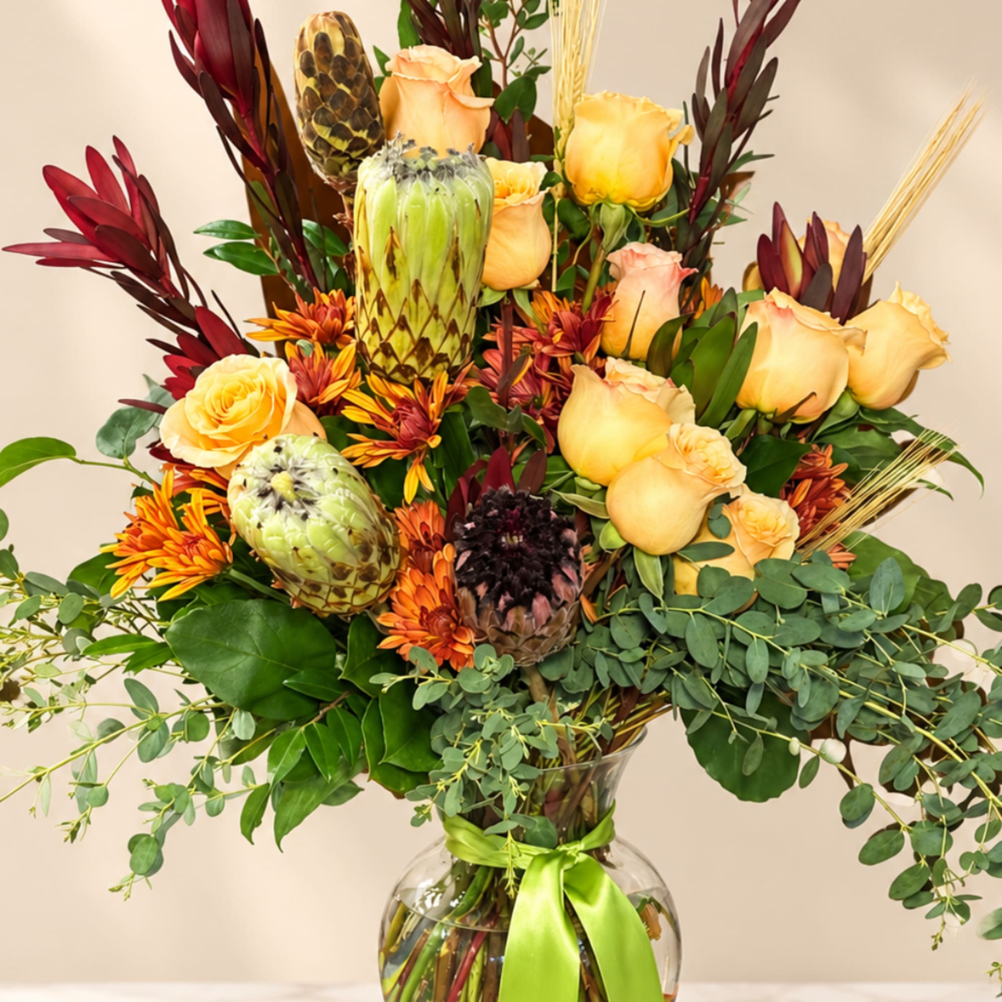 Bouquet of peach roses and protea in a glass vase with a green ribbon
