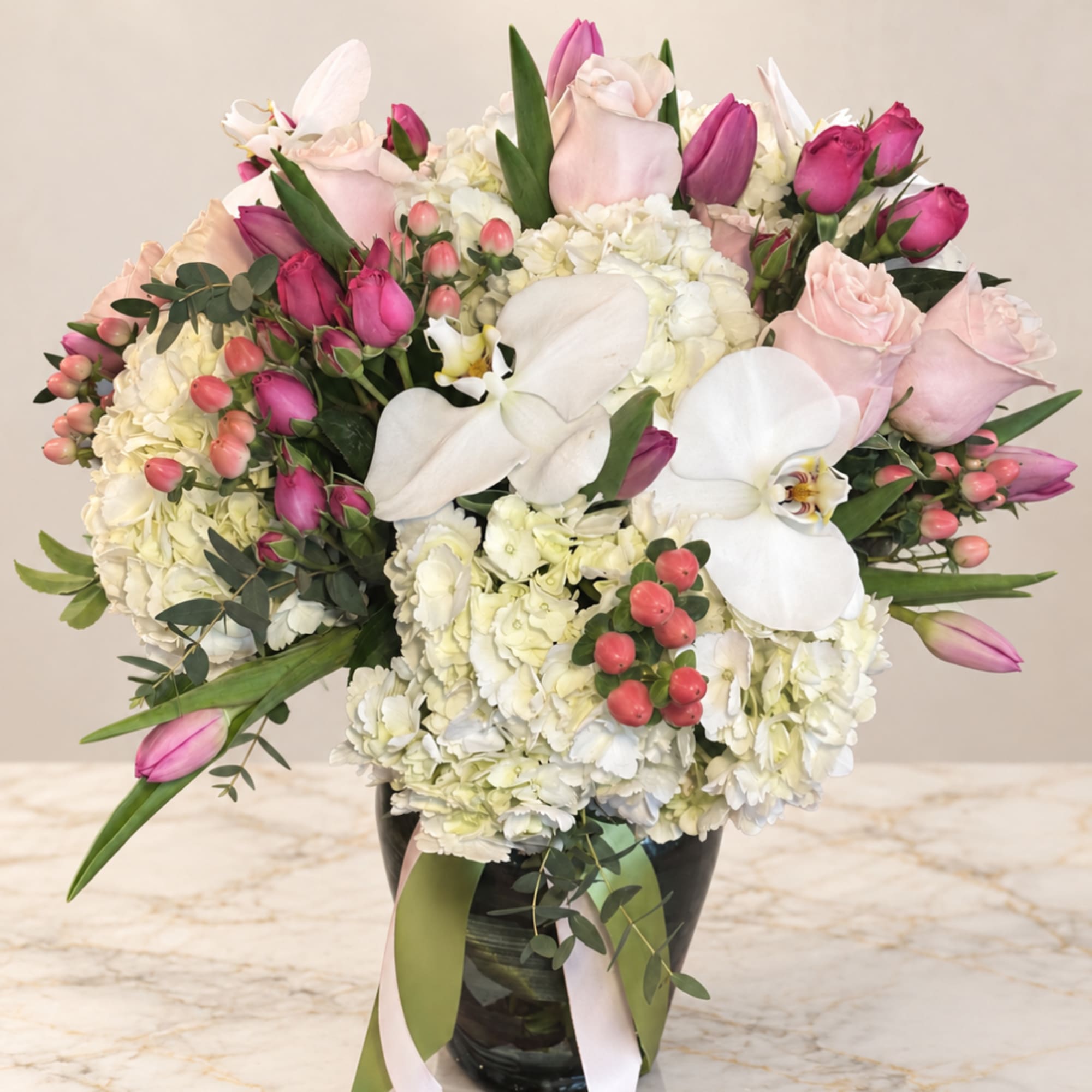 Pink and white floral arrangement in a black vase with orchids and roses