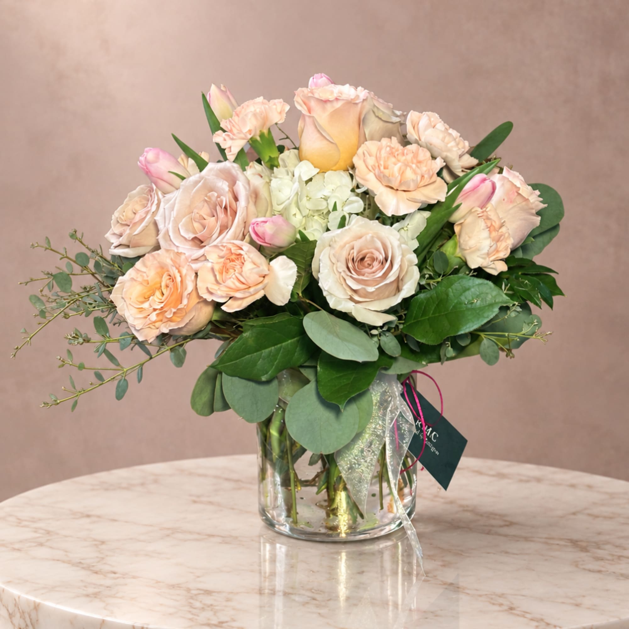 Peach and blush roses with carnations in a glass vase
