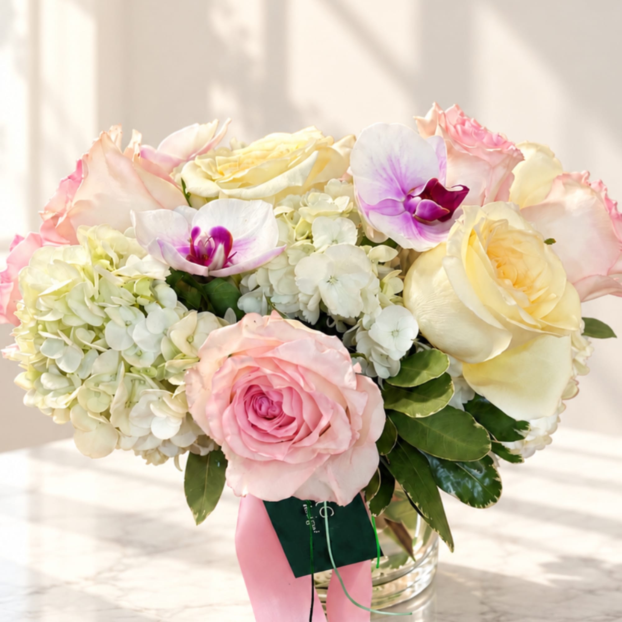 Pink and cream roses with white orchids in a glass vase
