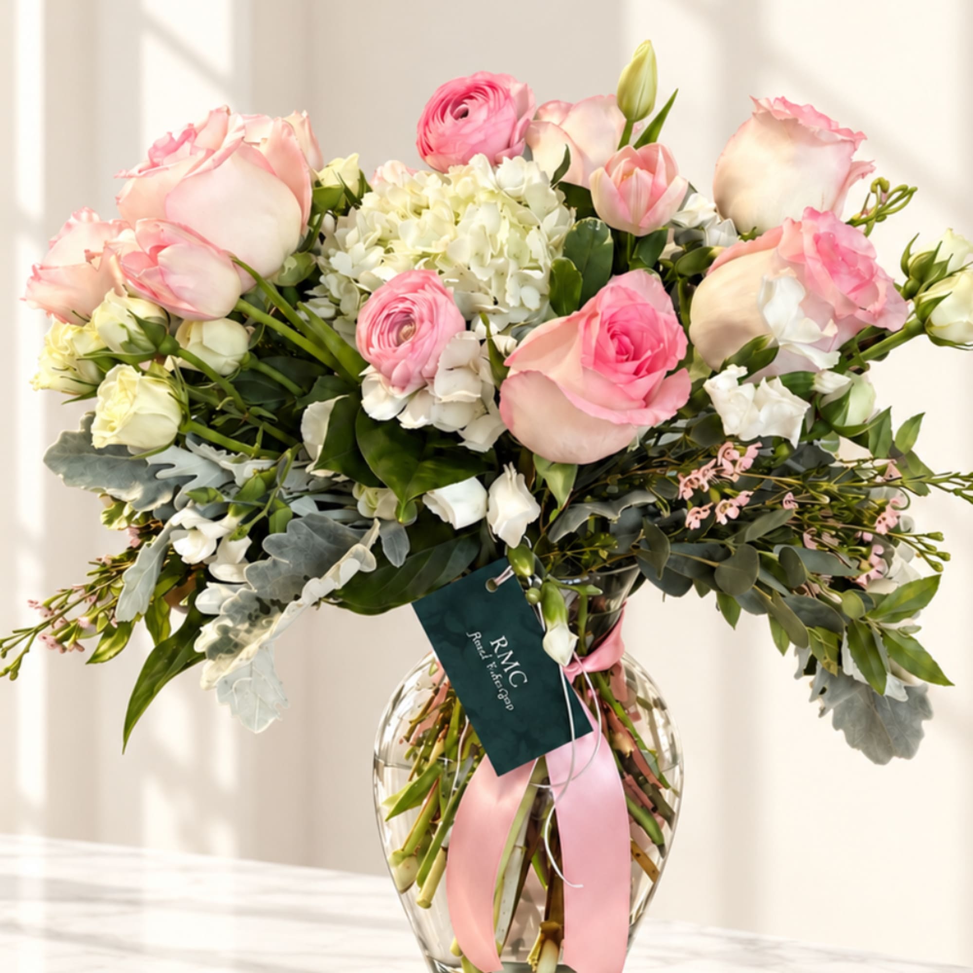 Pink roses and white blooms arranged in a clear glass vase with a pink ribbon