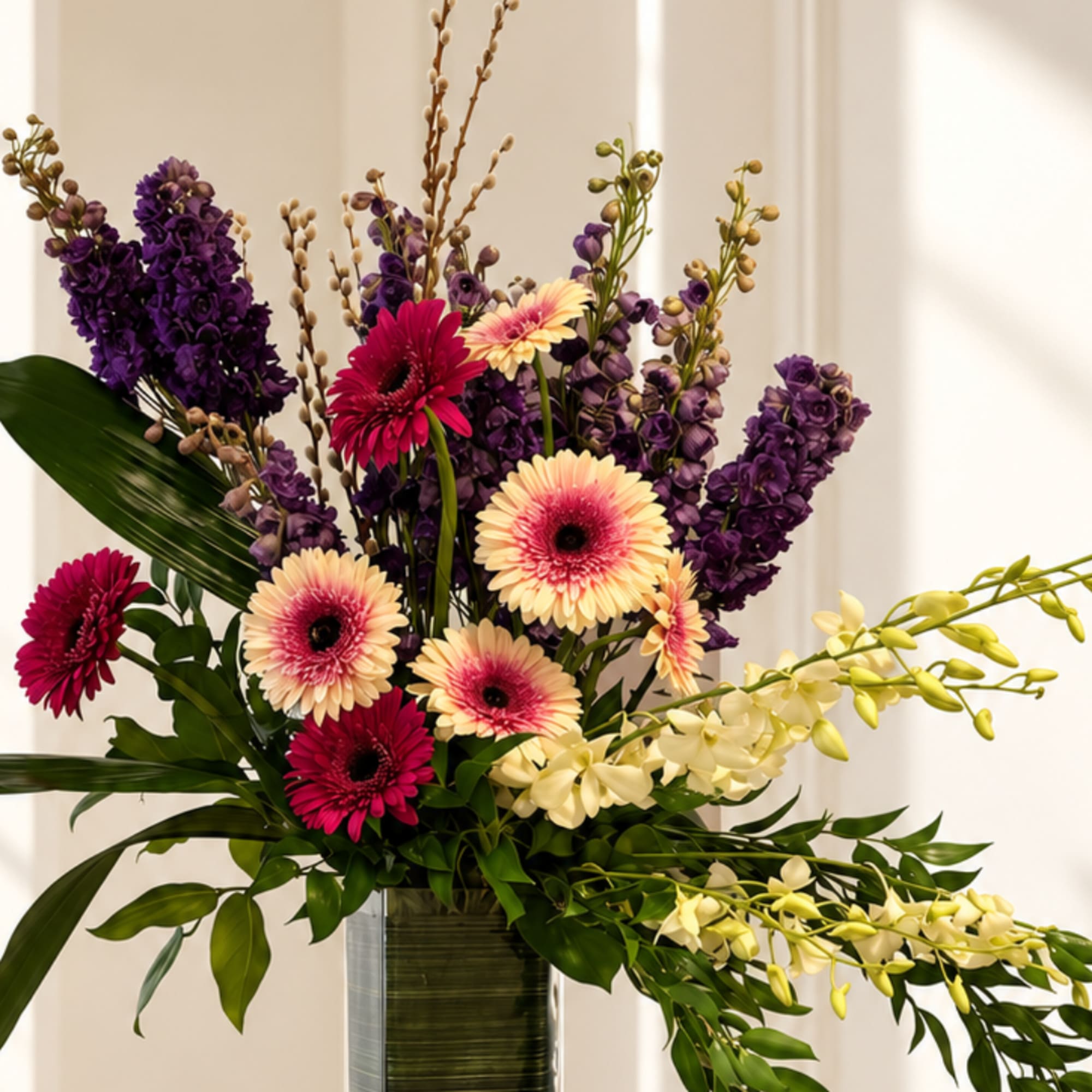Mixed bouquet with purple flowers, pink gerberas, and pale orchids in a glass vase