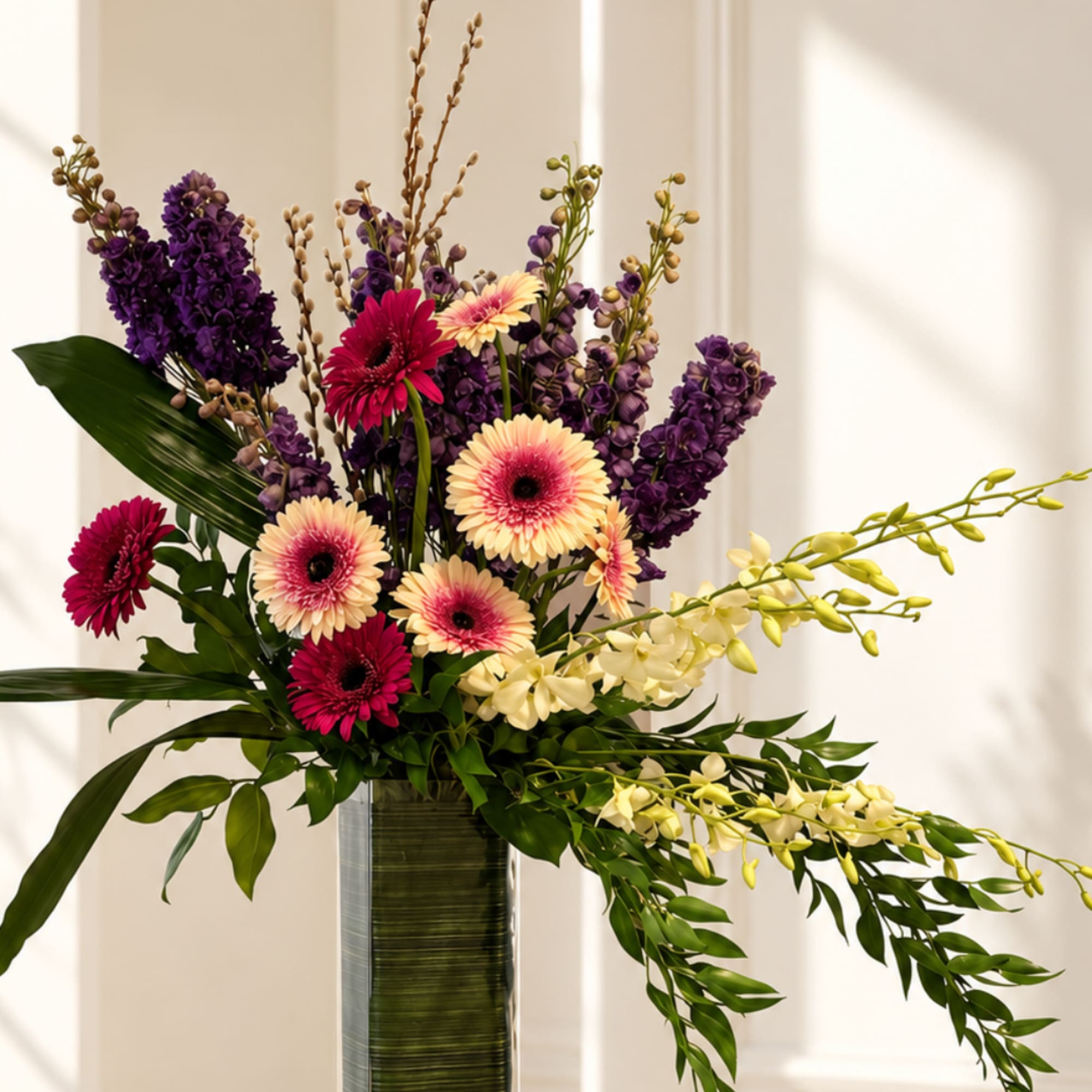 Tall floral arrangement with purple and pink blooms in a glass vase