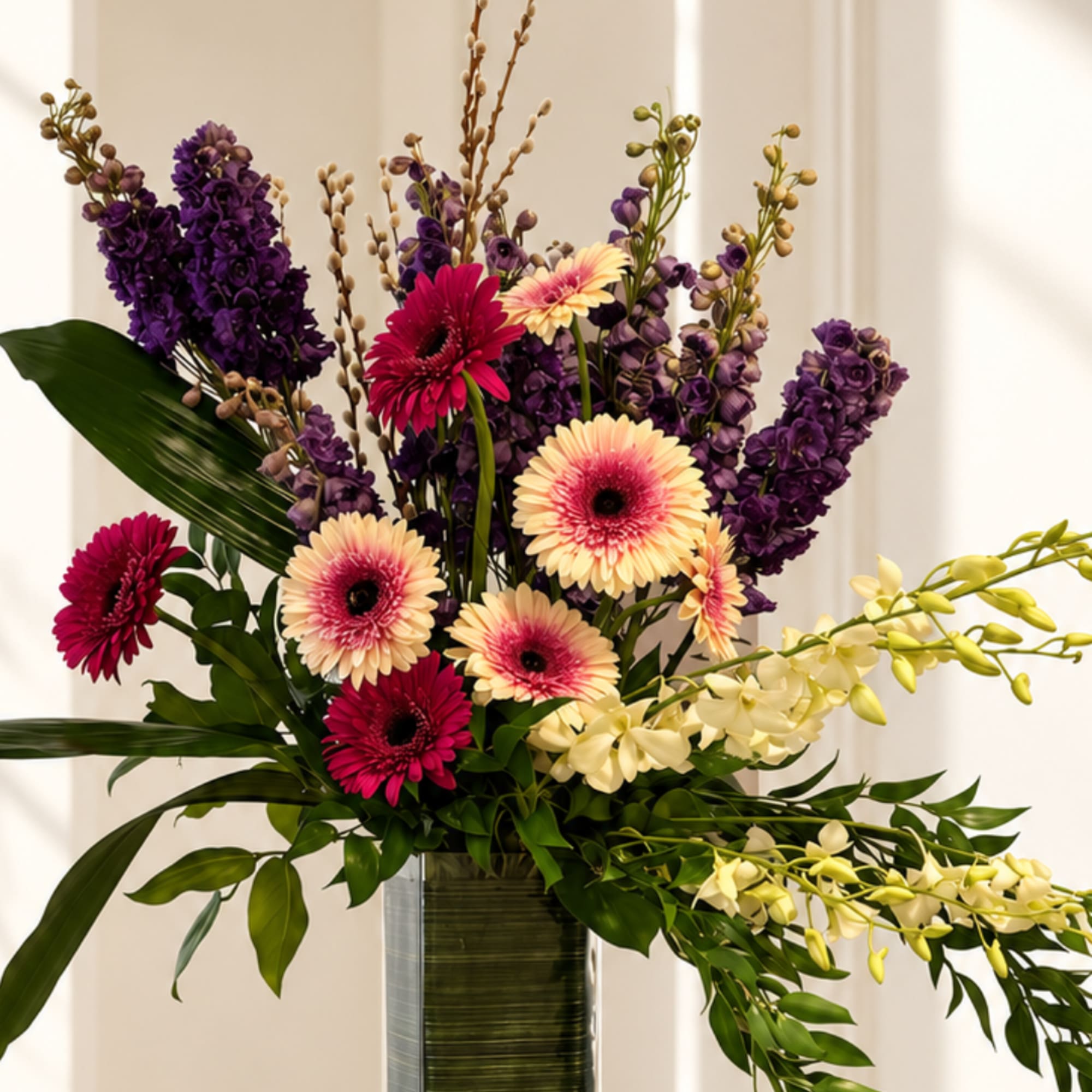 Tall mixed bouquet with purple blooms, pink gerberas, and pale orchids in a vase