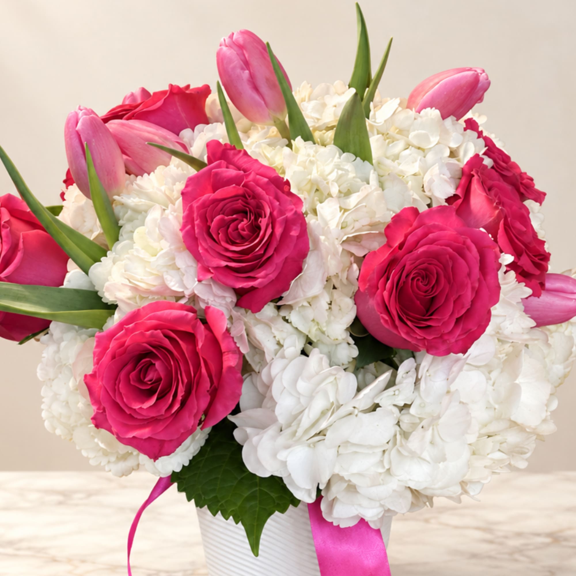 Pink roses and tulips arranged with white hydrangeas in a white vase