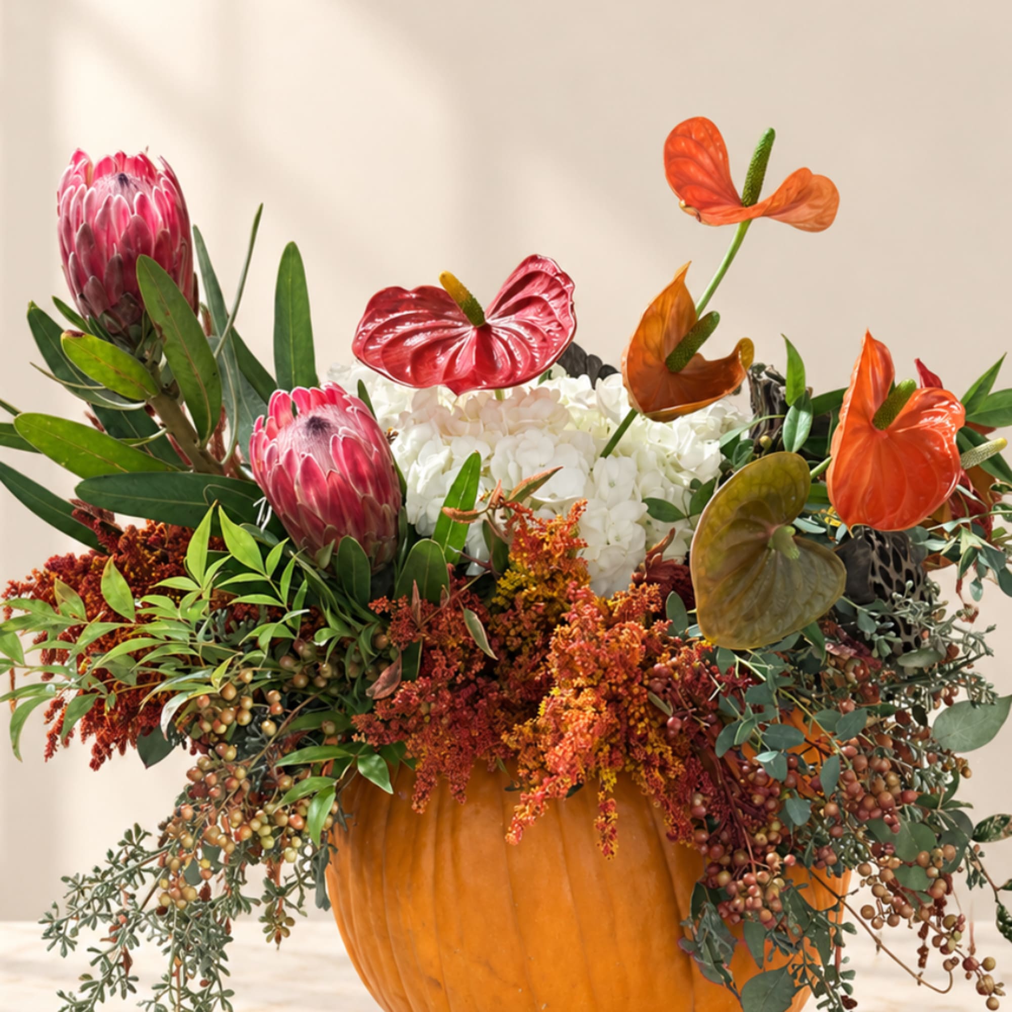 Tropical floral arrangement in a pumpkin-shaped container with orange and pink blooms