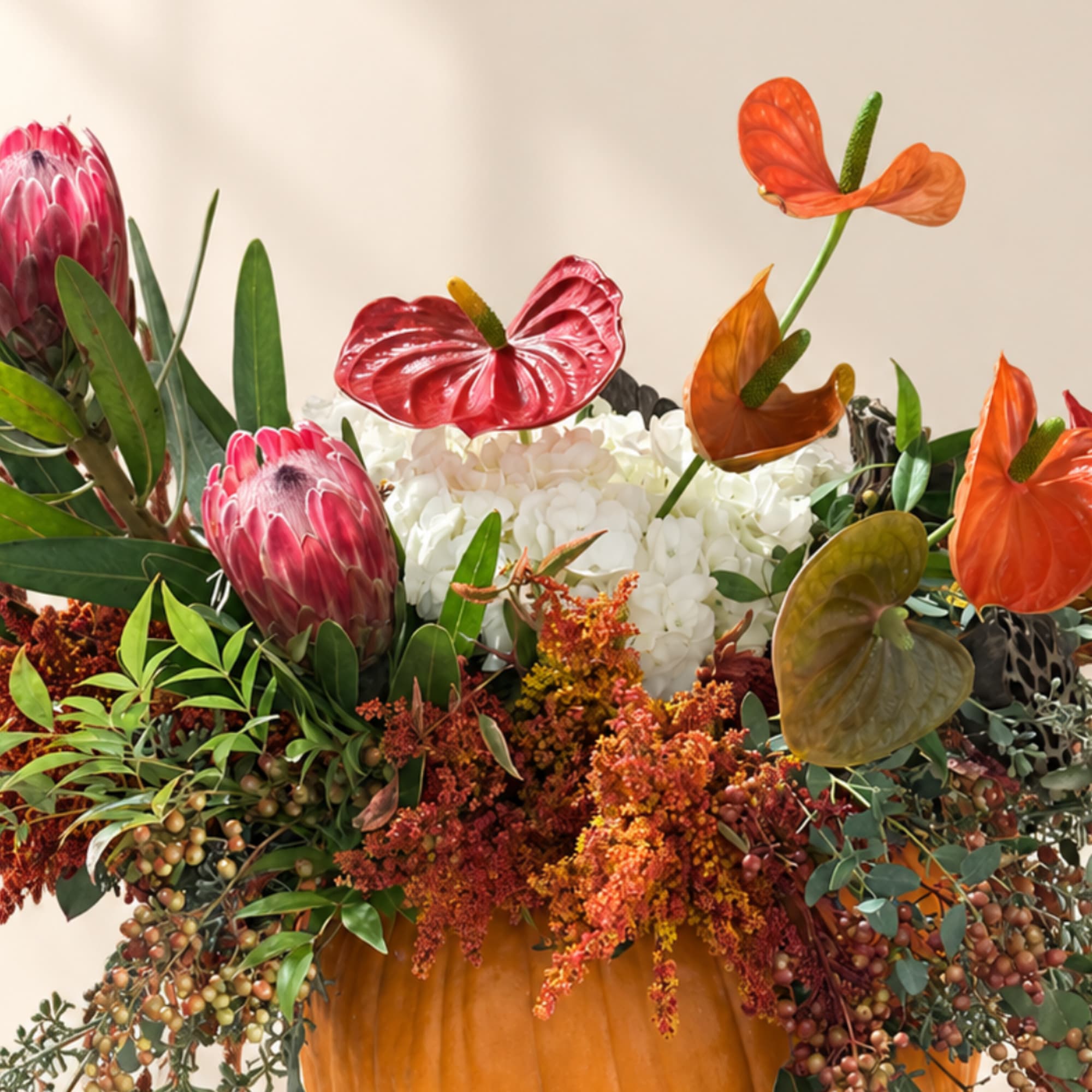Tropical floral arrangement with anthuriums and protea in a pumpkin vase