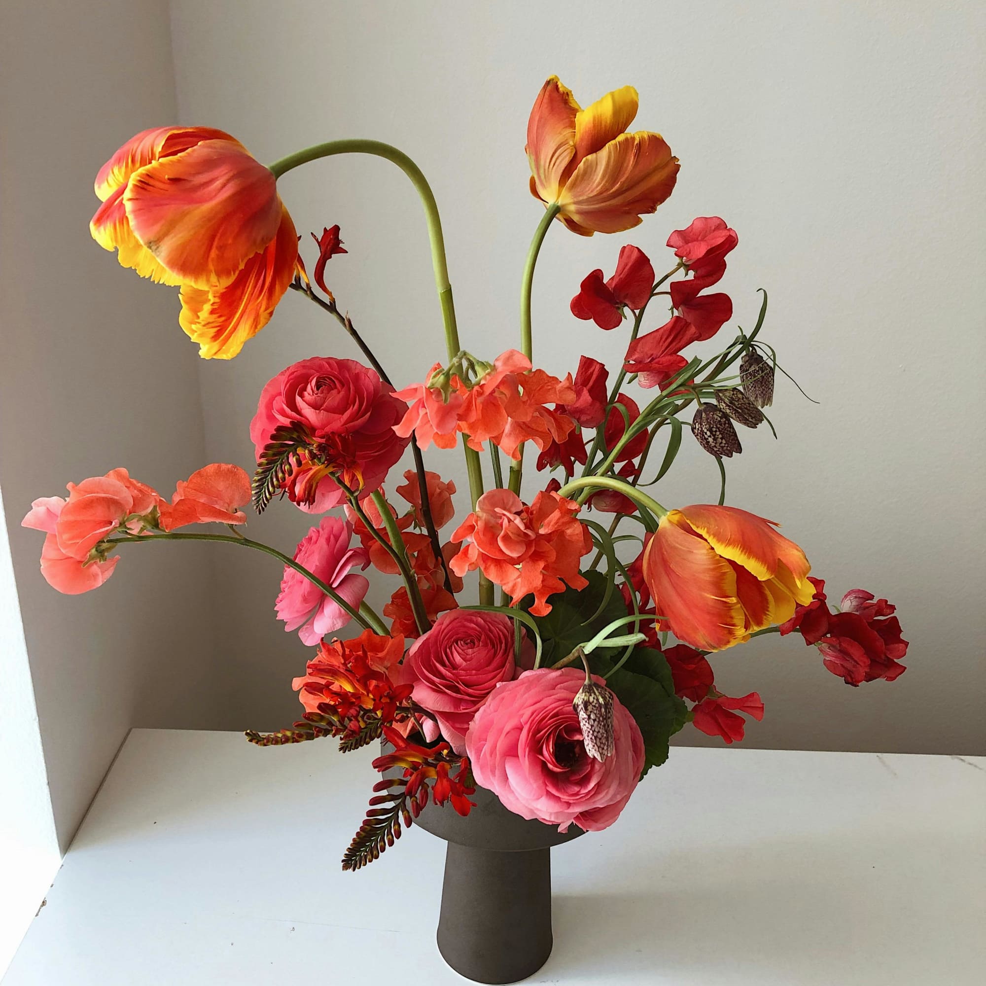 Bright mixed bouquet in a dark vase with orange tulips and pink ranunculus