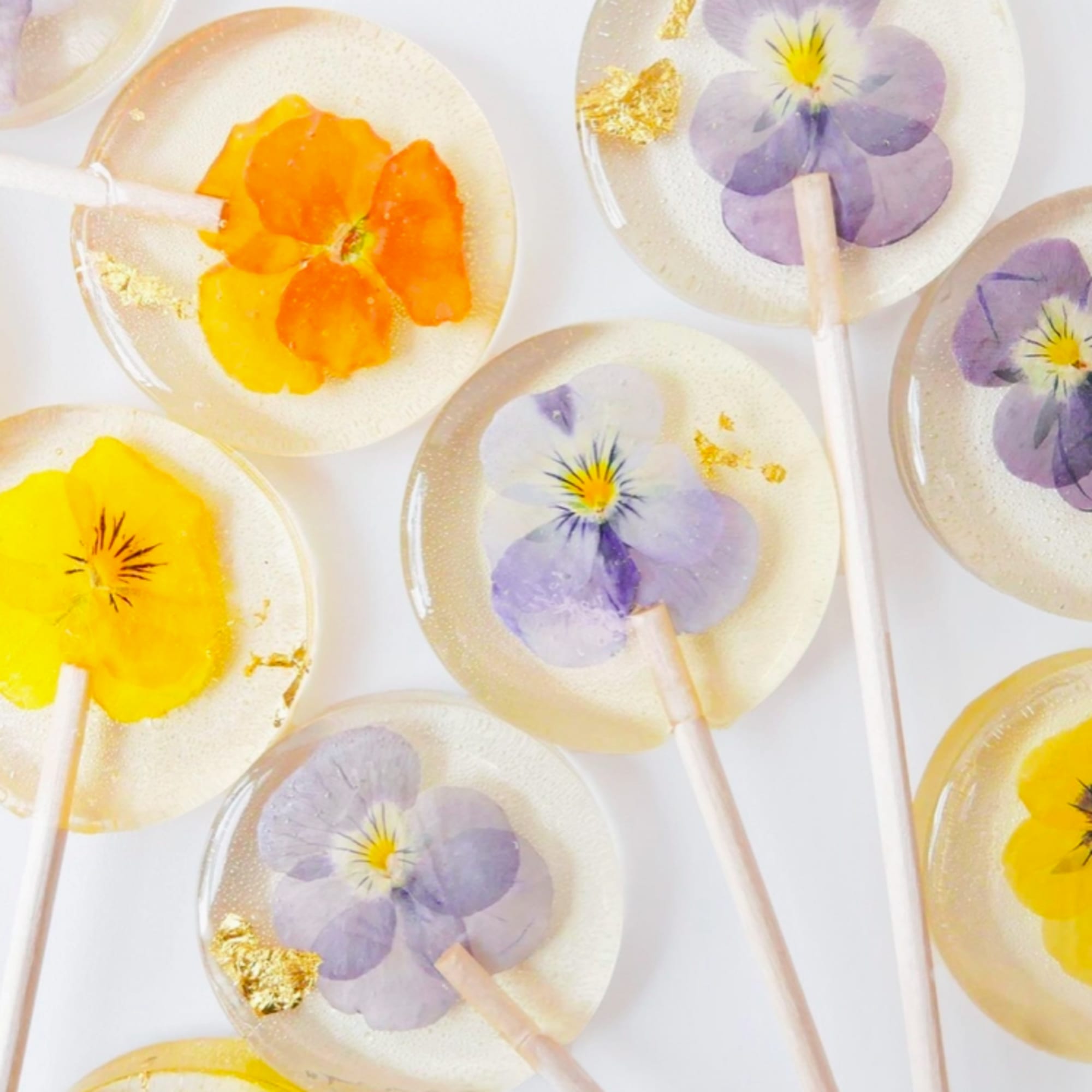 Clear lollipops with pressed yellow and lavender flowers and gold leaf on a white background