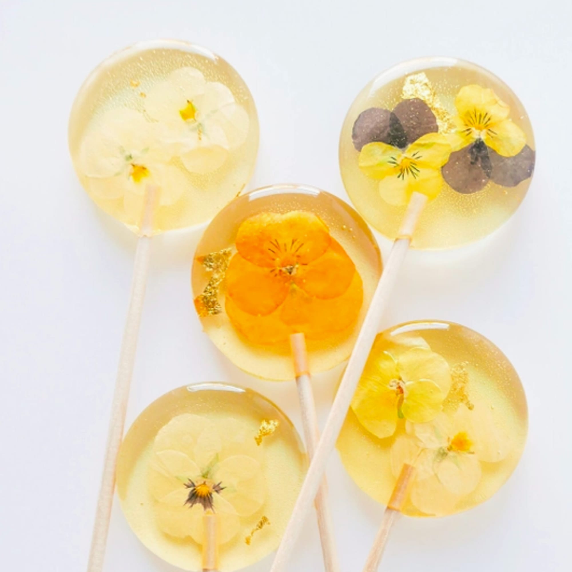 Set of clear round lollipops with yellow flowers and gold flakes inside.