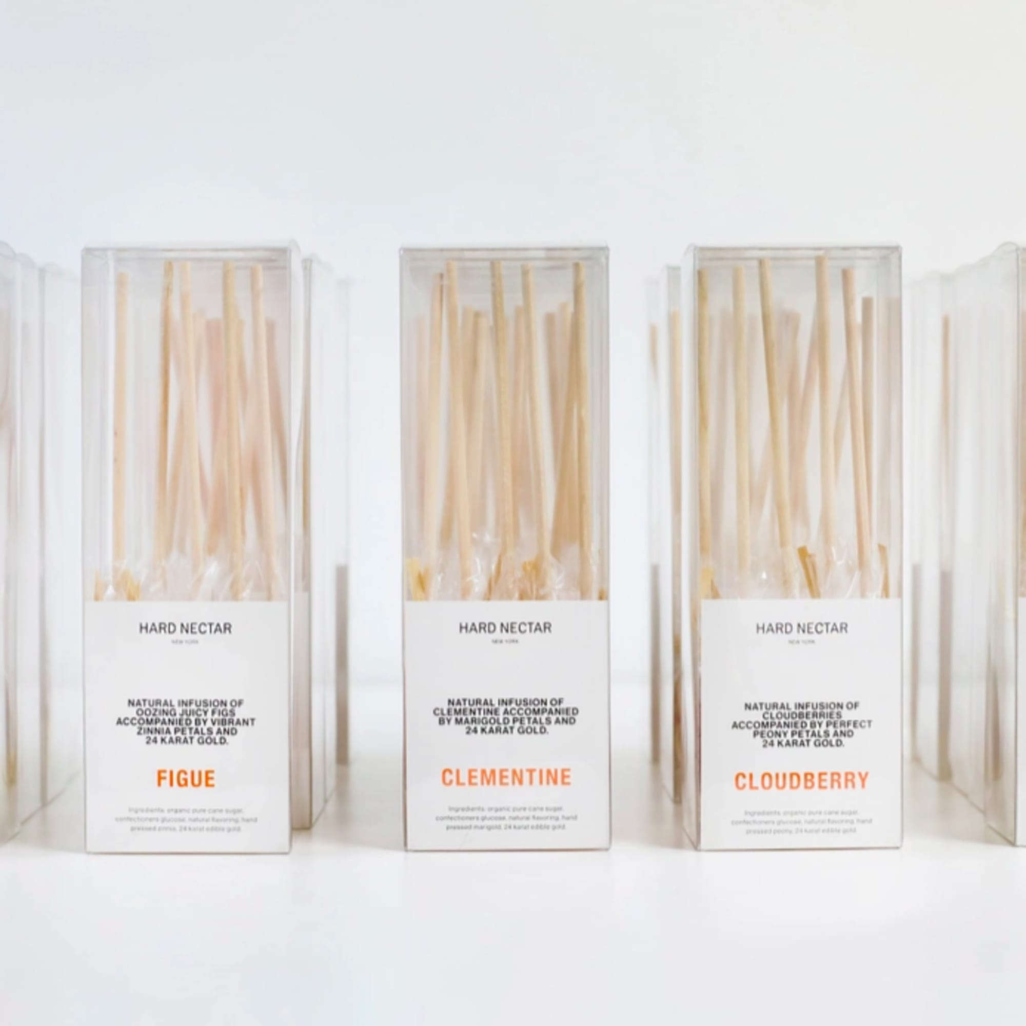 Set of five clear boxes filled with slender beige stir sticks labeled with different flavors.