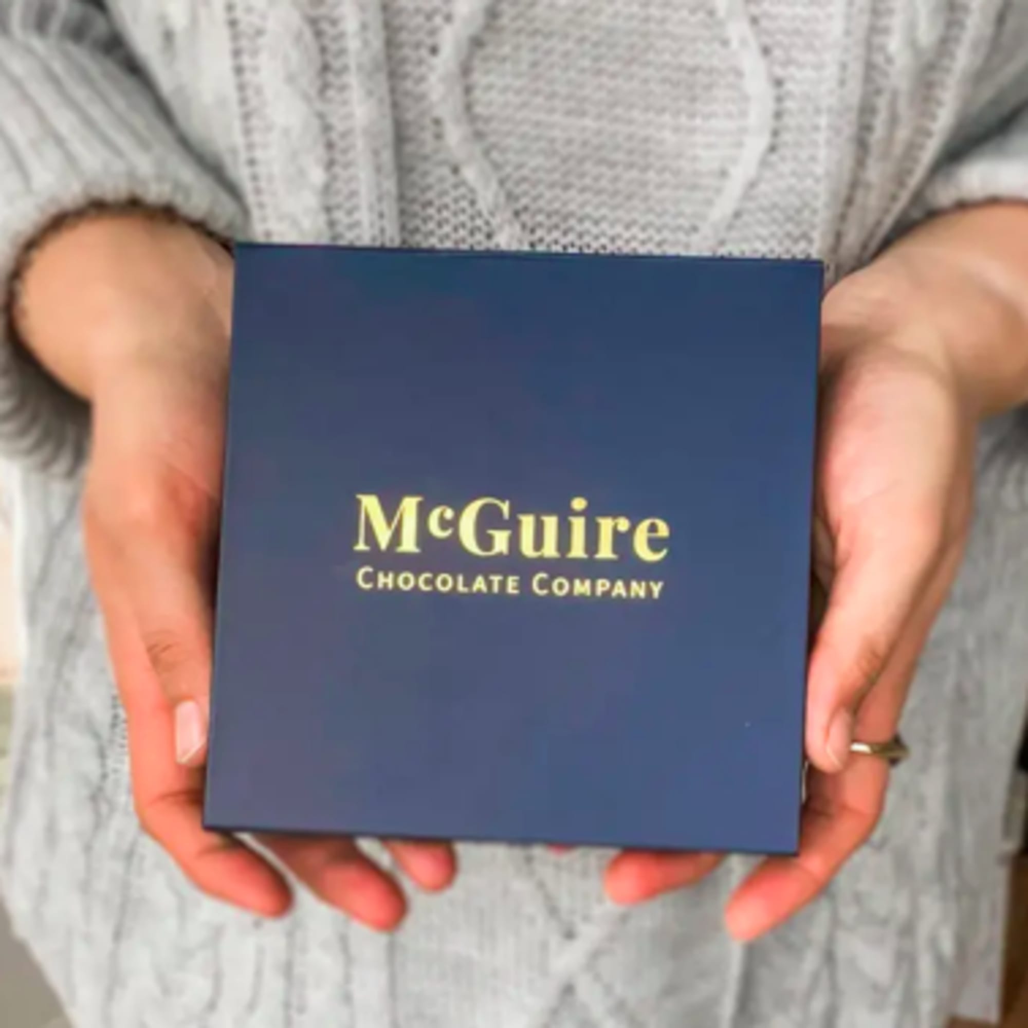 Hands holding a blue McGuire Chocolate Company gift box