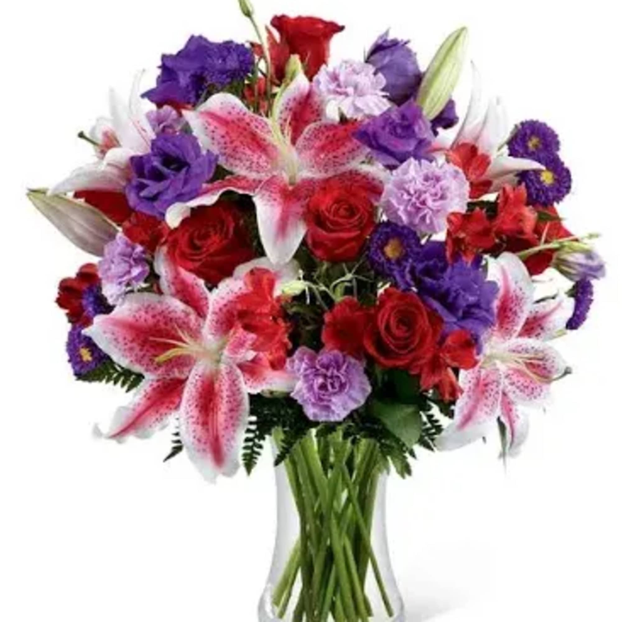 Arrangement of pink lilies, red roses, and purple blooms in a clear glass vase