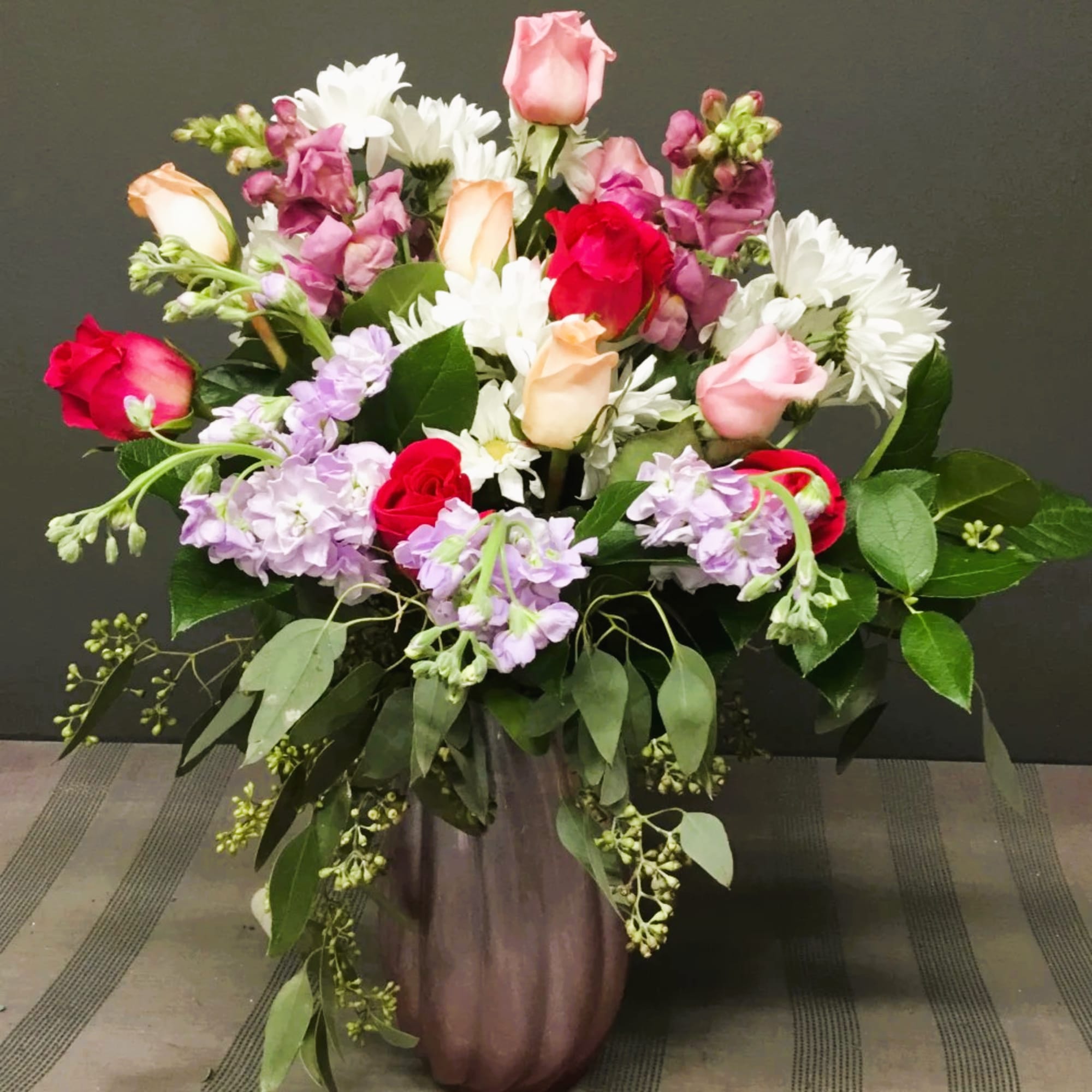 Mixed bouquet of roses, daisies, and purple blooms in a tall vase