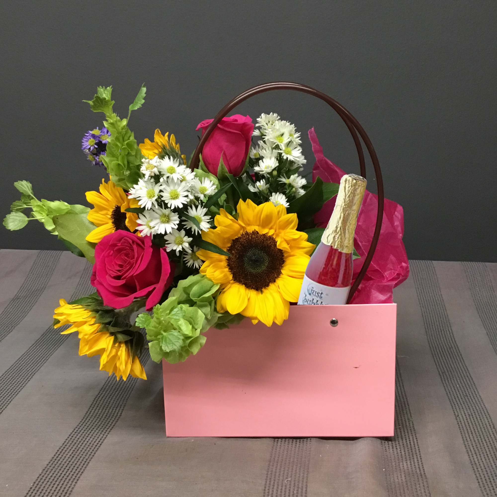 Pink gift bag with mixed flowers and a small bottle of sparkling drink