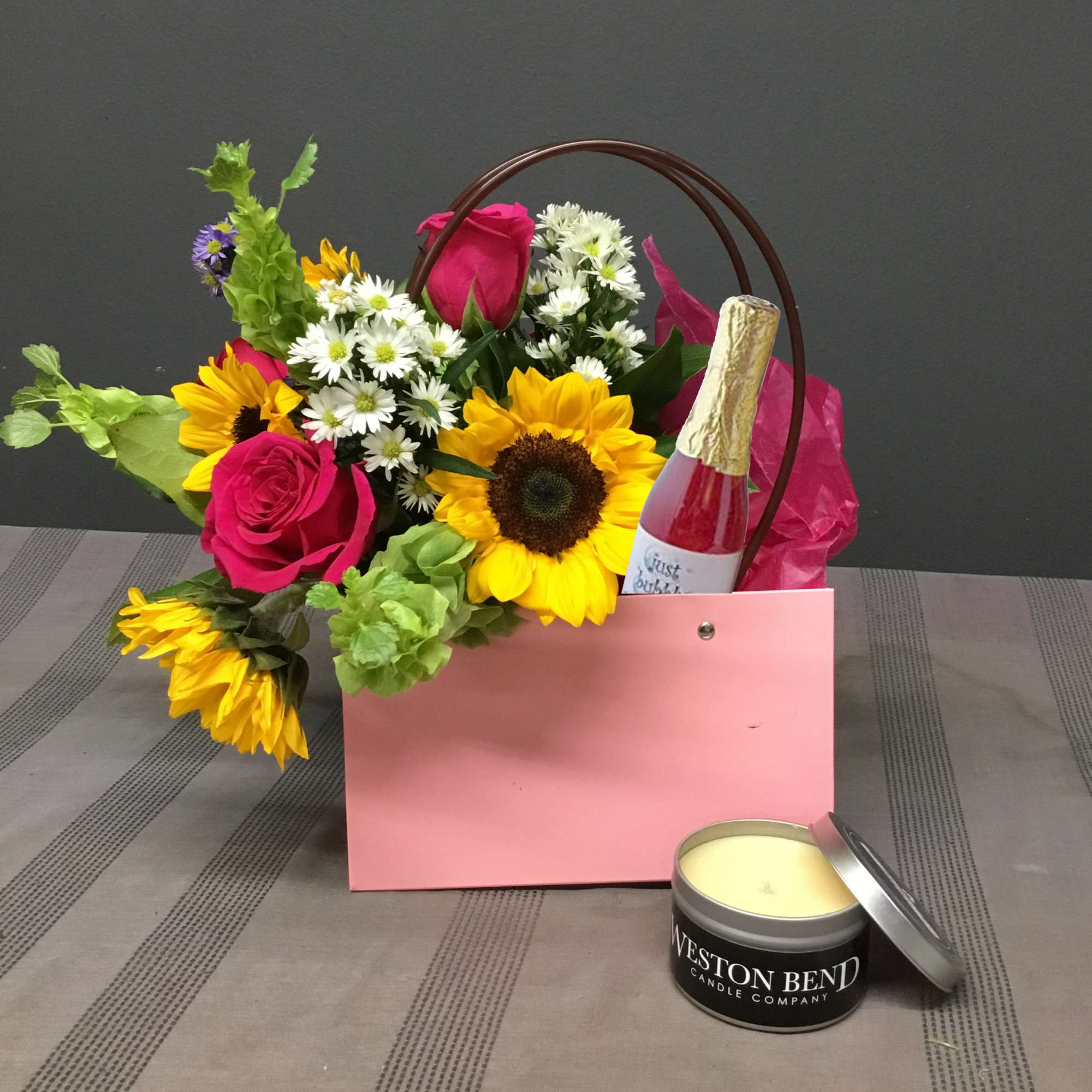 Mixed bouquet in a pink gift bag with a candle and bottle of sparkling drink